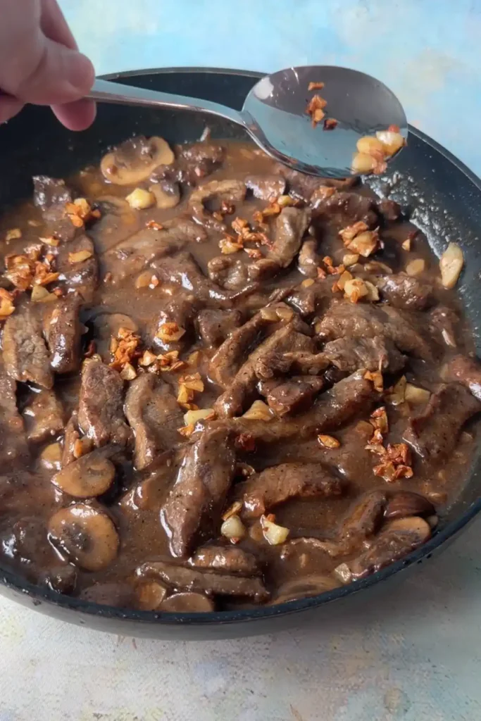 Spoon sprinkling crispy fried garlic over garlic pepper beef and mushroom gravy.