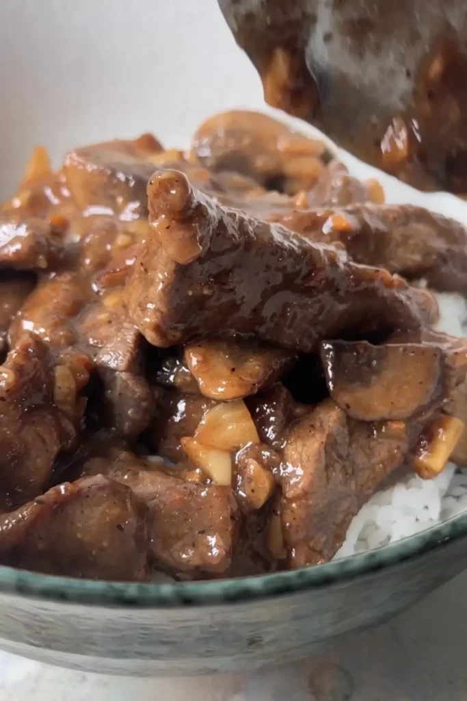 Garlic pepper beef with mushrooms and glossy gravy served over steamed white rice.
