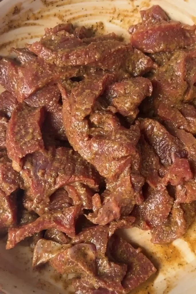 Marinated beef slices coated in dark garlic pepper sauce in a bowl.