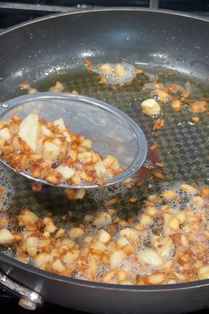 Crispy golden brown garlic pieces being scooped out of oil with a mesh strainer.