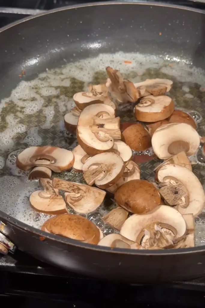 Sliced brown mushrooms added to garlic-infused butter in a skillet.