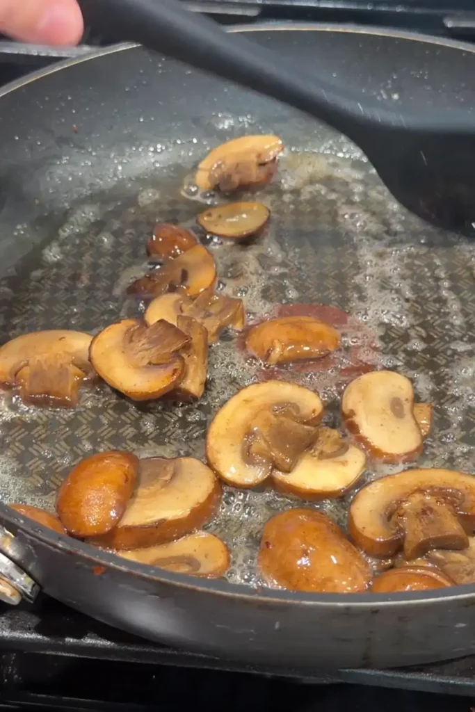 Mushrooms sautéing in butter until browned and glossy in a pan.