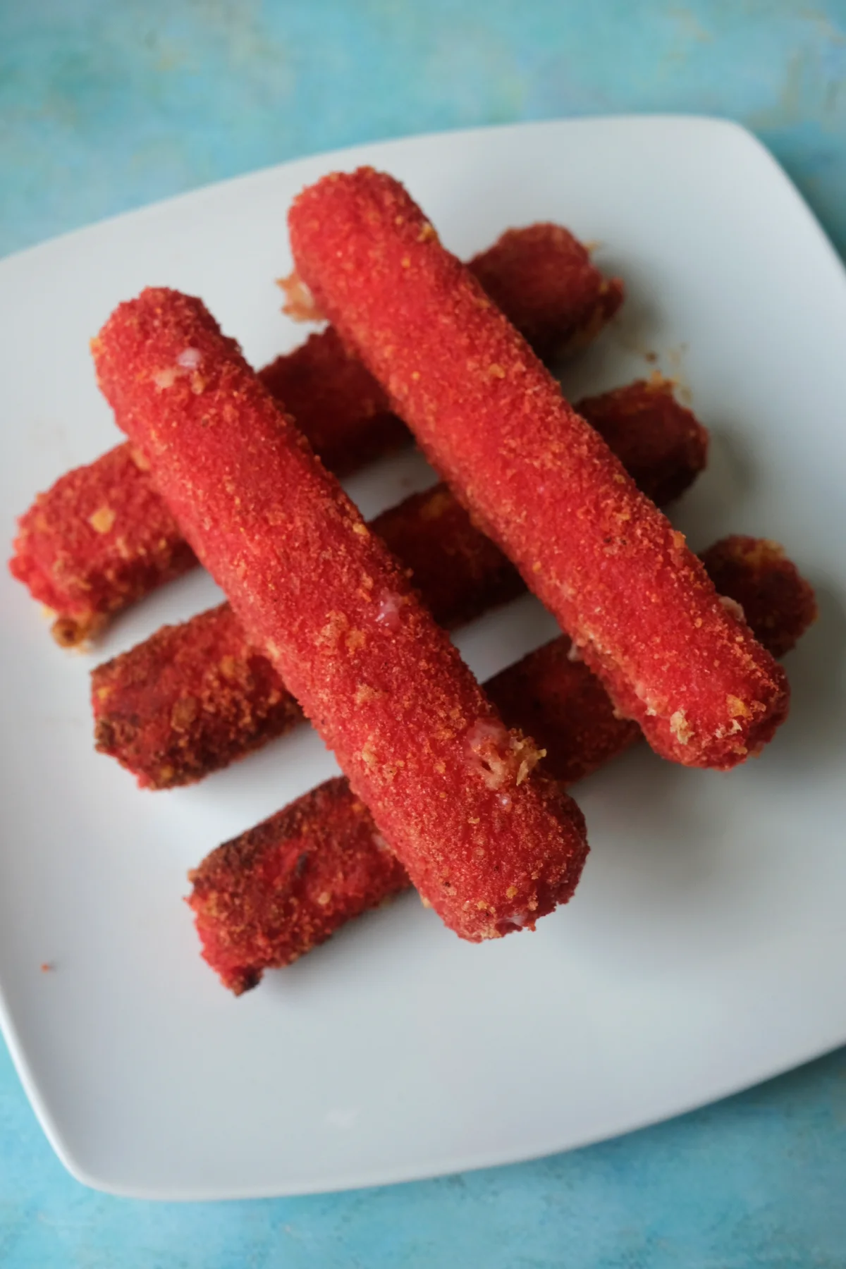 Crispy Hot Cheetos mozzarella sticks stacked on a white plate with bright red crunchy coating.