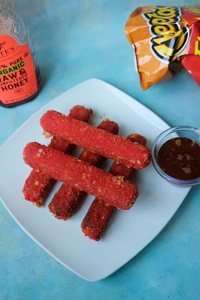 Hot Cheeto mozzarella cheese sticks served with hot honey dipping sauce on a white plate.