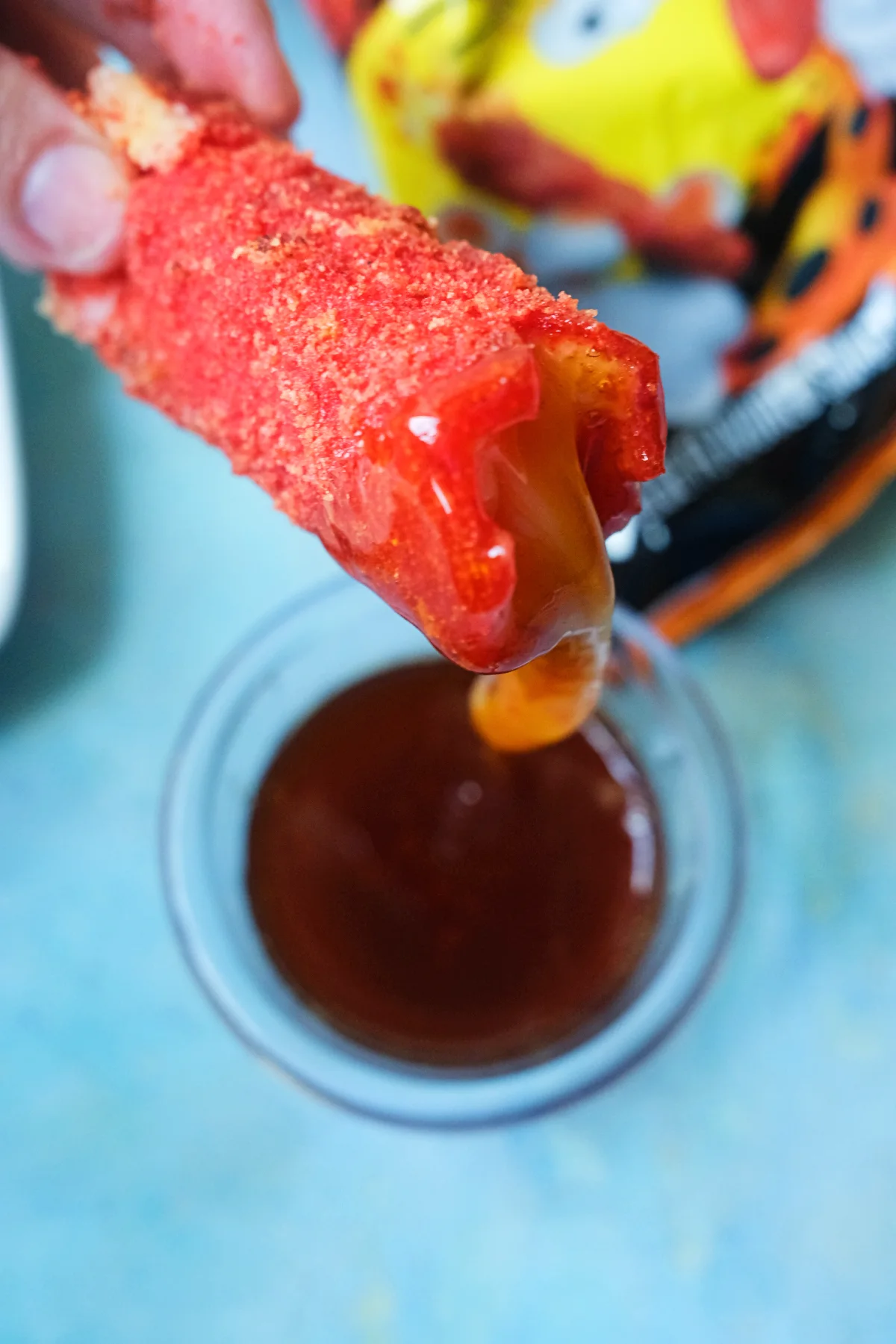 Hand holding a Hot Cheeto mozzarella stick dipped in hot honey with melted cheese stretching out.