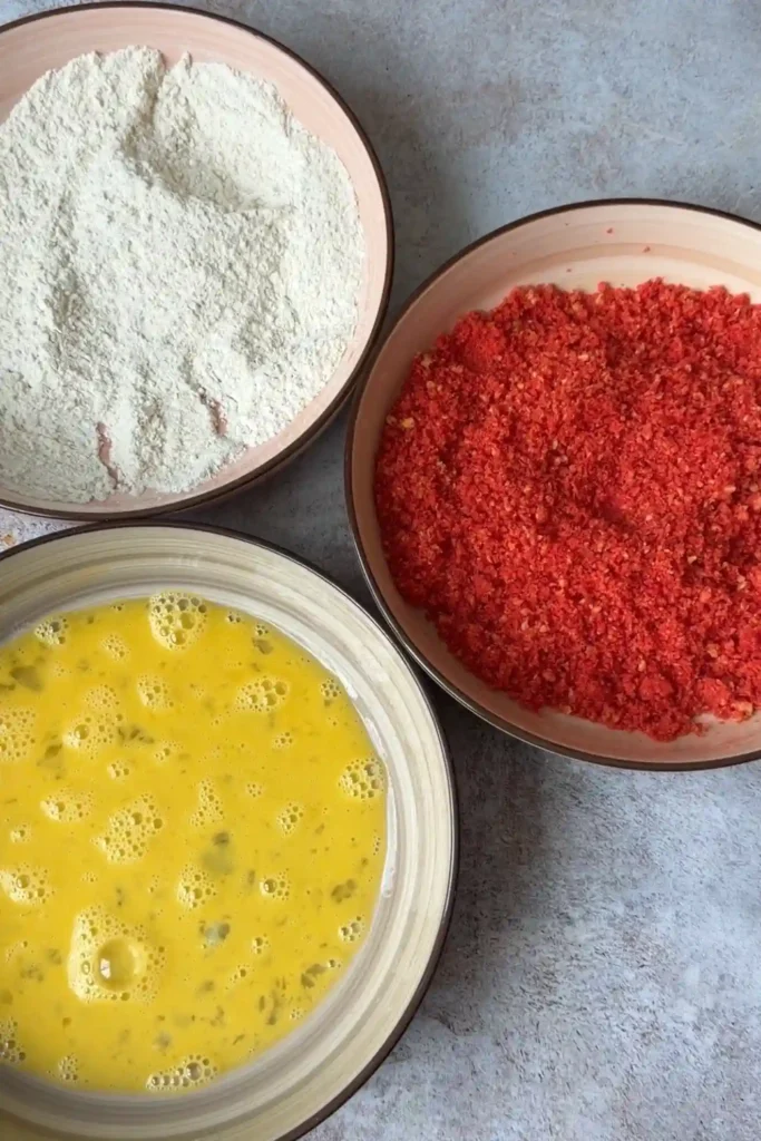 Three breading stations with seasoned flour, beaten eggs, and crushed Hot Cheetos for mozzarella sticks.