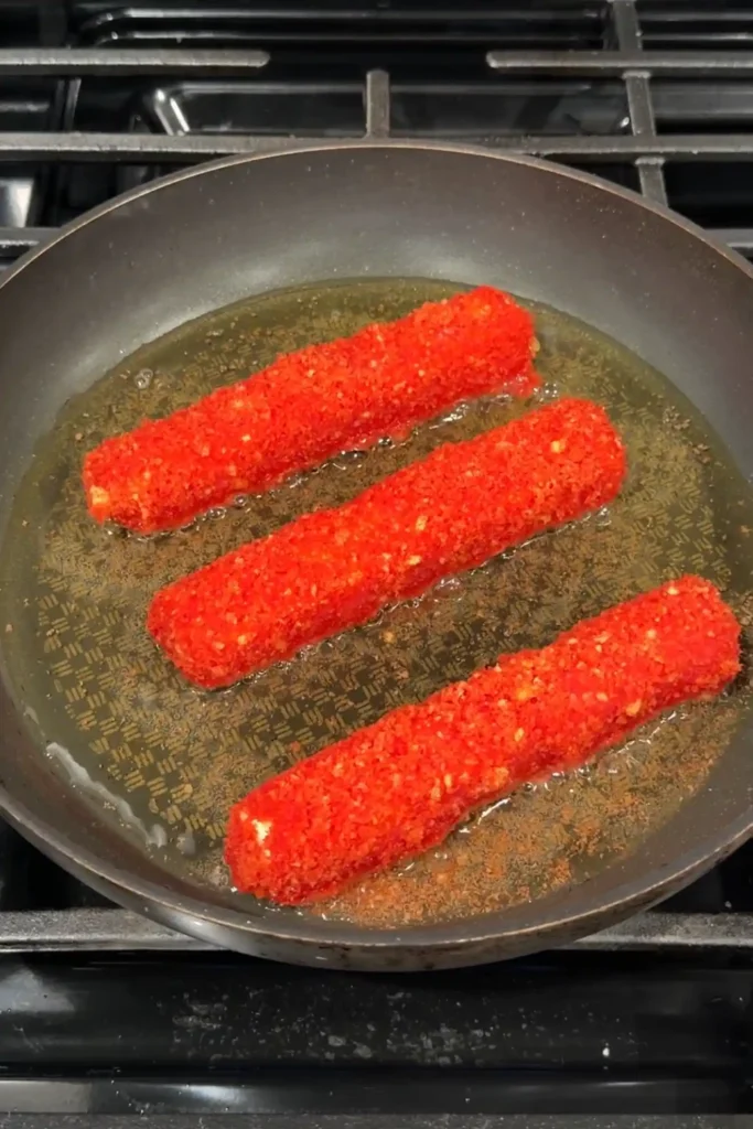 Hot Cheetos mozzarella sticks shallow frying in oil in a skillet on the stovetop.
