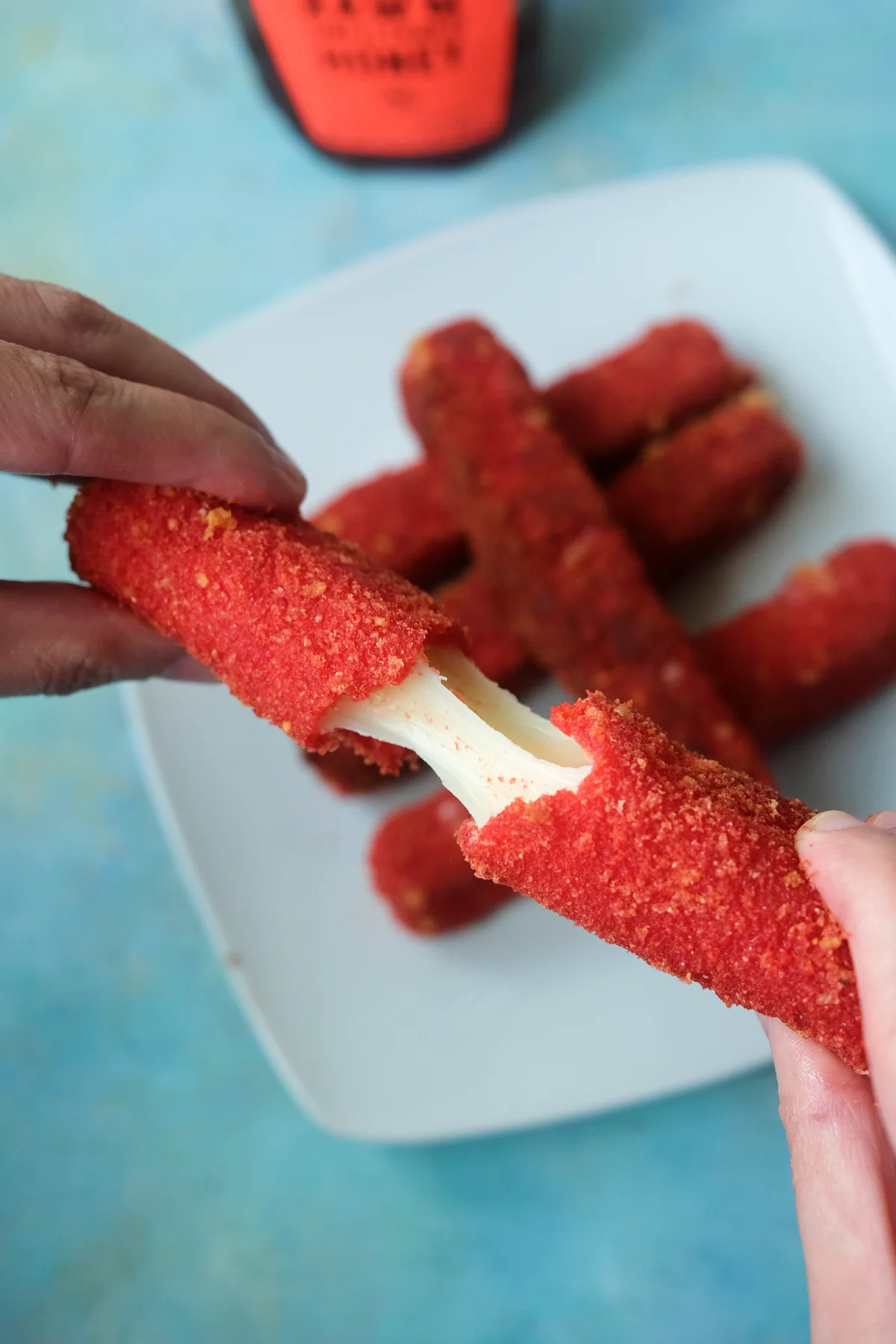 Close-up of Hot Cheetos mozzarella sticks being pulled apart with a gooey melted cheese stretch in the center.