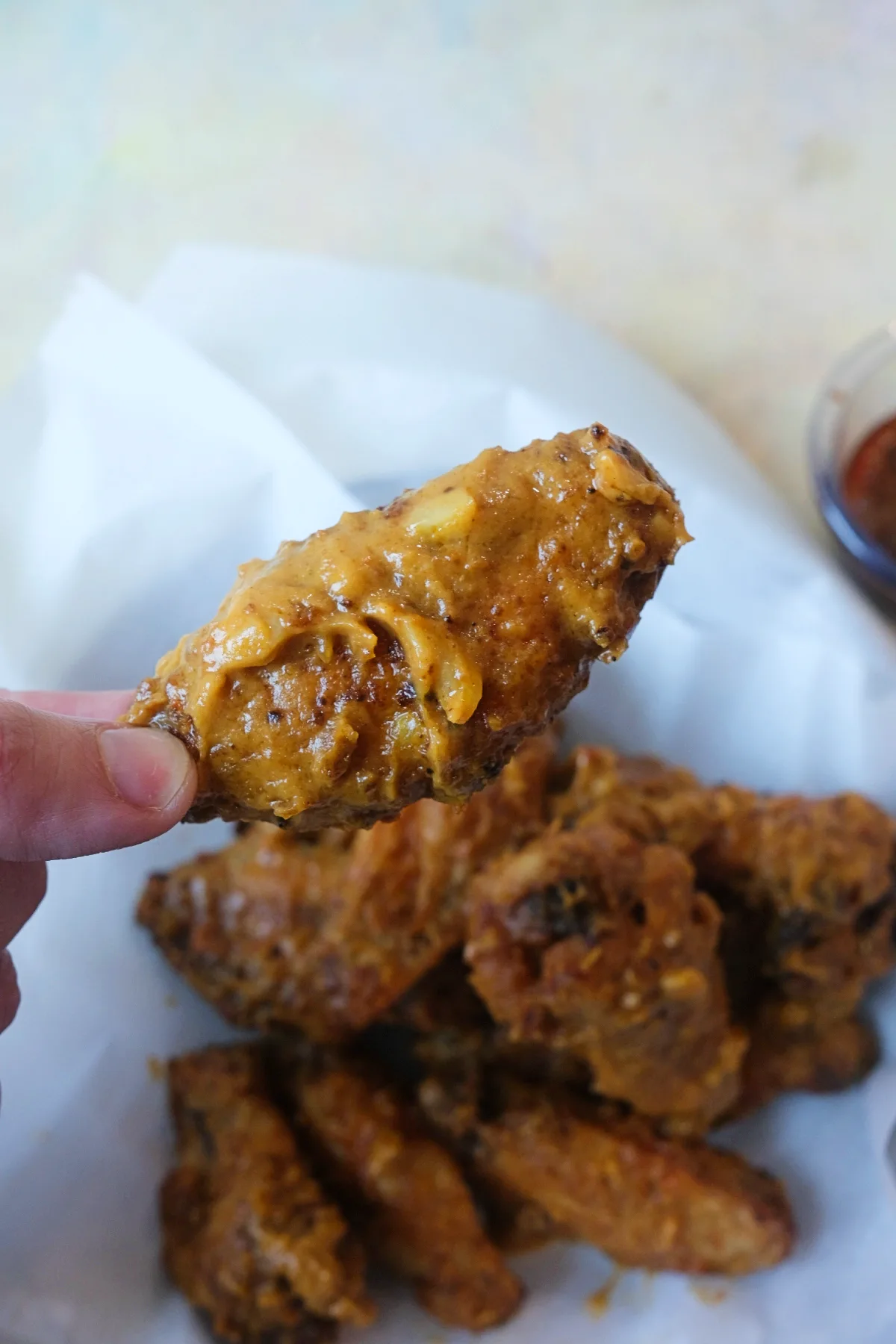 Hand holding a crispy air fryer chicken wing coated in creamy kare kare sauce.