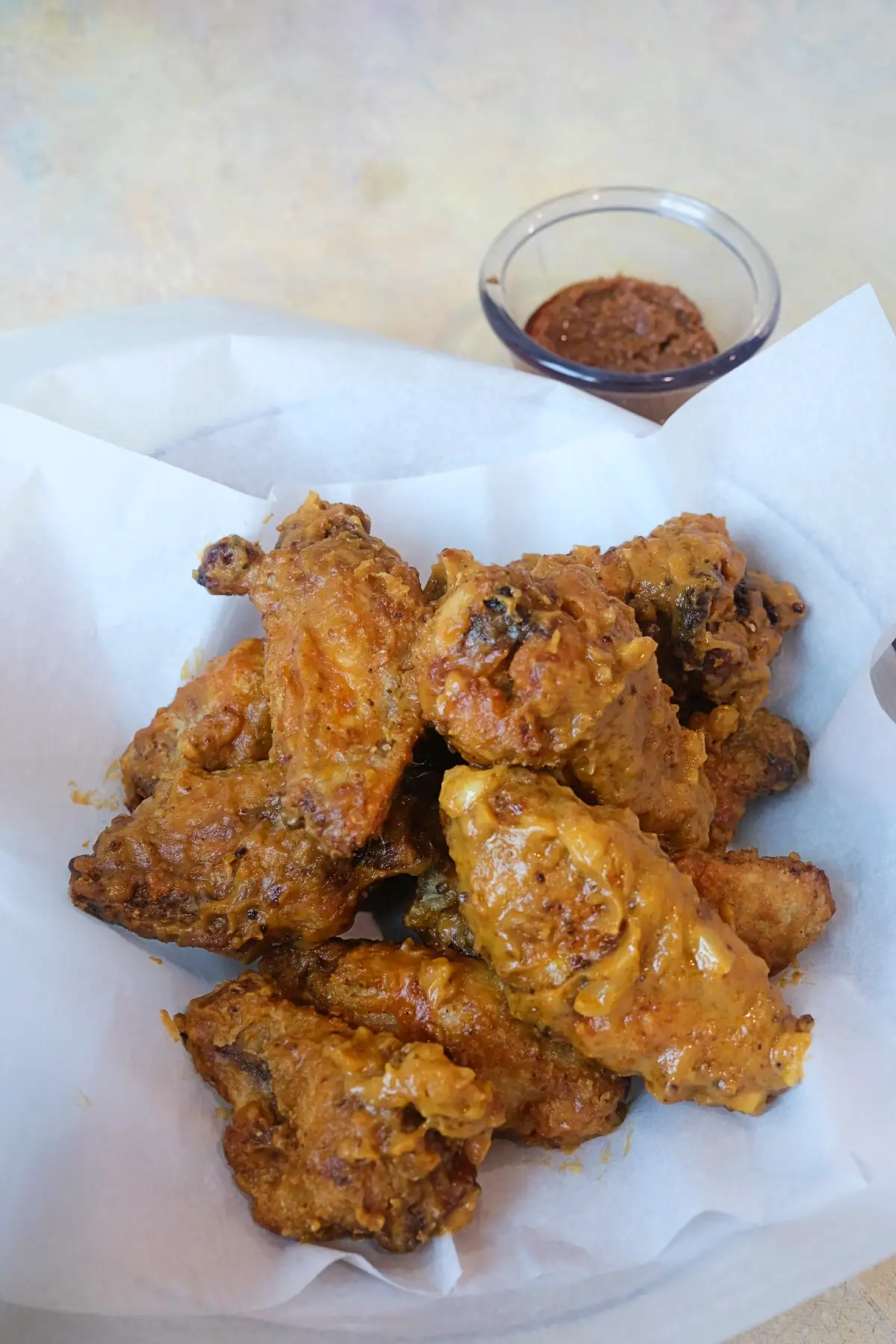 Kare kare chicken wings served with a side of bagoong dipping sauce on parchment paper.