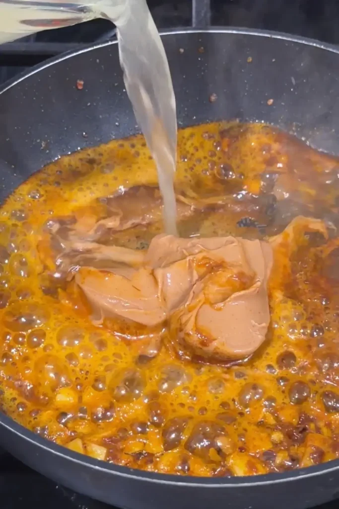 Chicken broth being poured into peanut butter and annatto mixture for kare kare sauce.