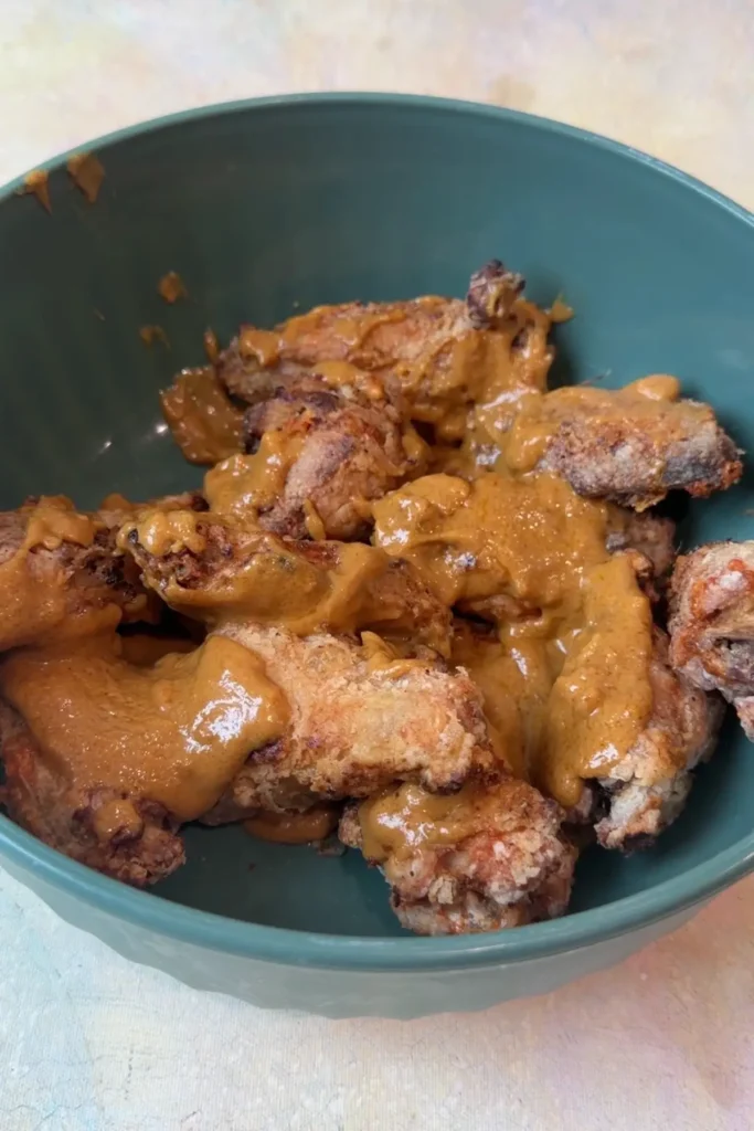Crispy air fryer chicken wings drizzled with homemade kare kare peanut sauce in a mixing bowl.