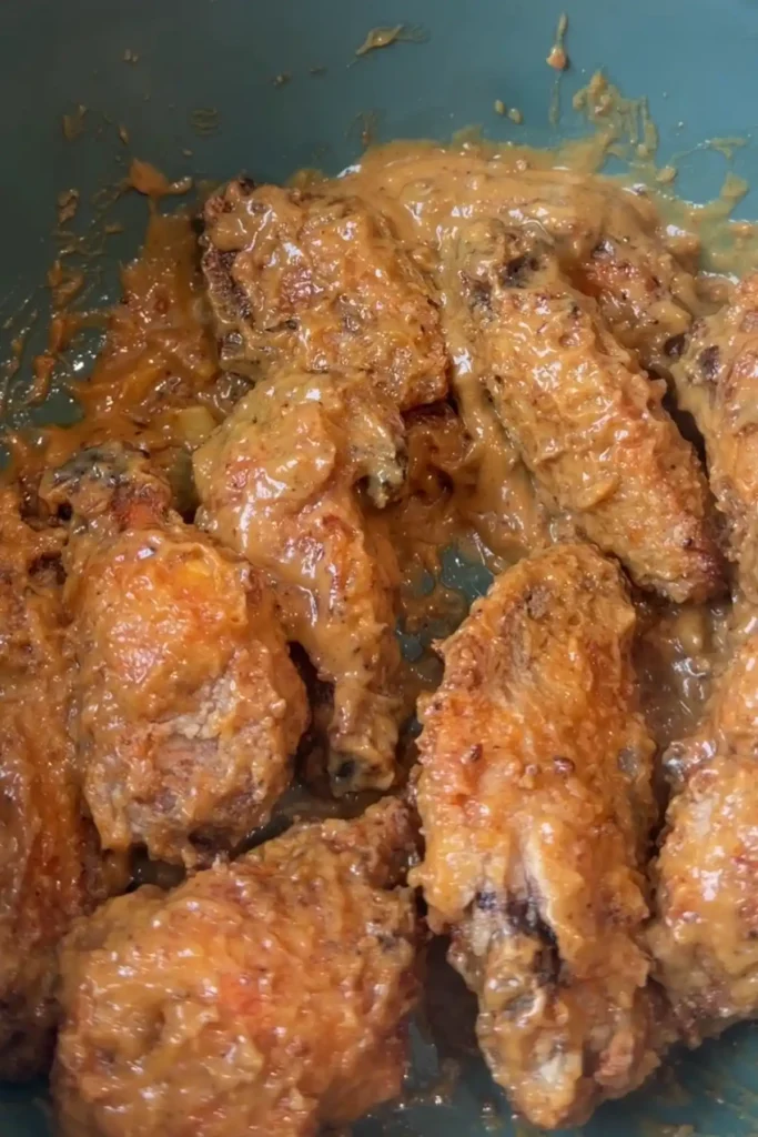 Close-up of crispy chicken wings coated in creamy kare kare sauce.