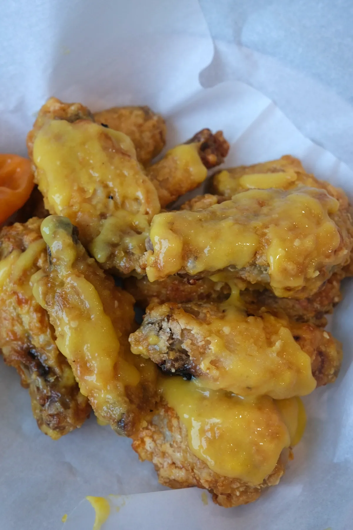 Crispy air fryer mango habanero wings piled in a parchment-lined bowl with glossy yellow sauce on top.