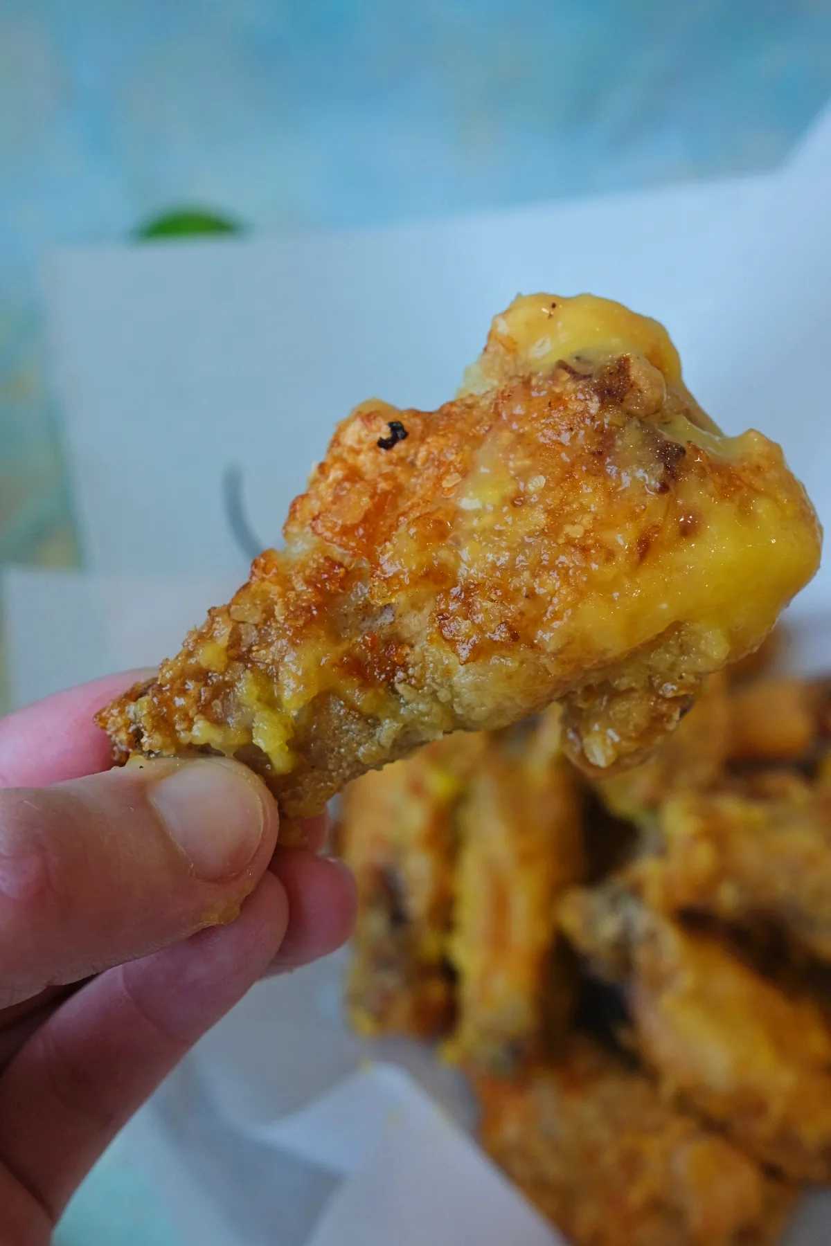 Close-up of a crispy mango habanero chicken wing held by hand with golden coating and sauce.
