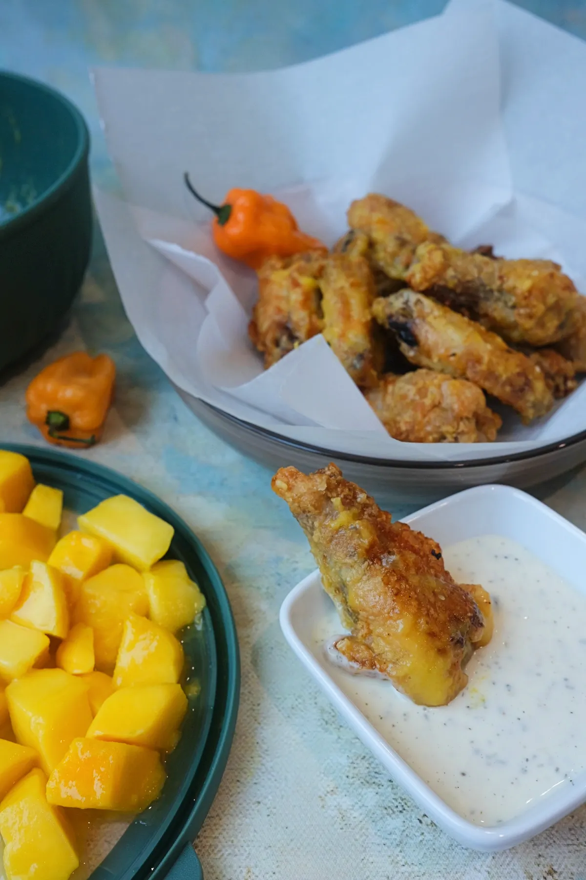 Crispy mango habanero wing dipped into creamy ranch sauce with mango chunks and habanero peppers in the background.
