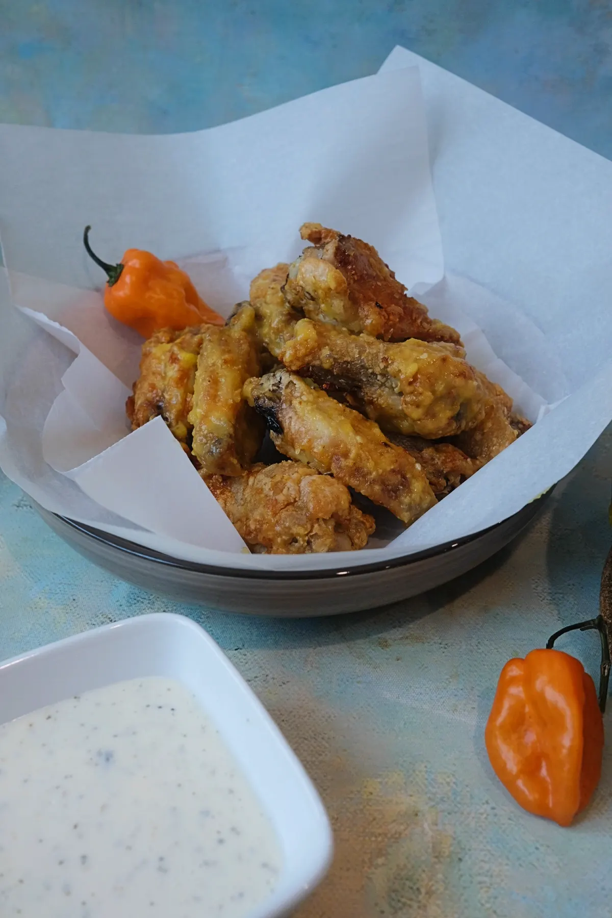 Crispy air fryer mango habanero wings in a parchment-lined serving bowl with a habanero pepper on the side.