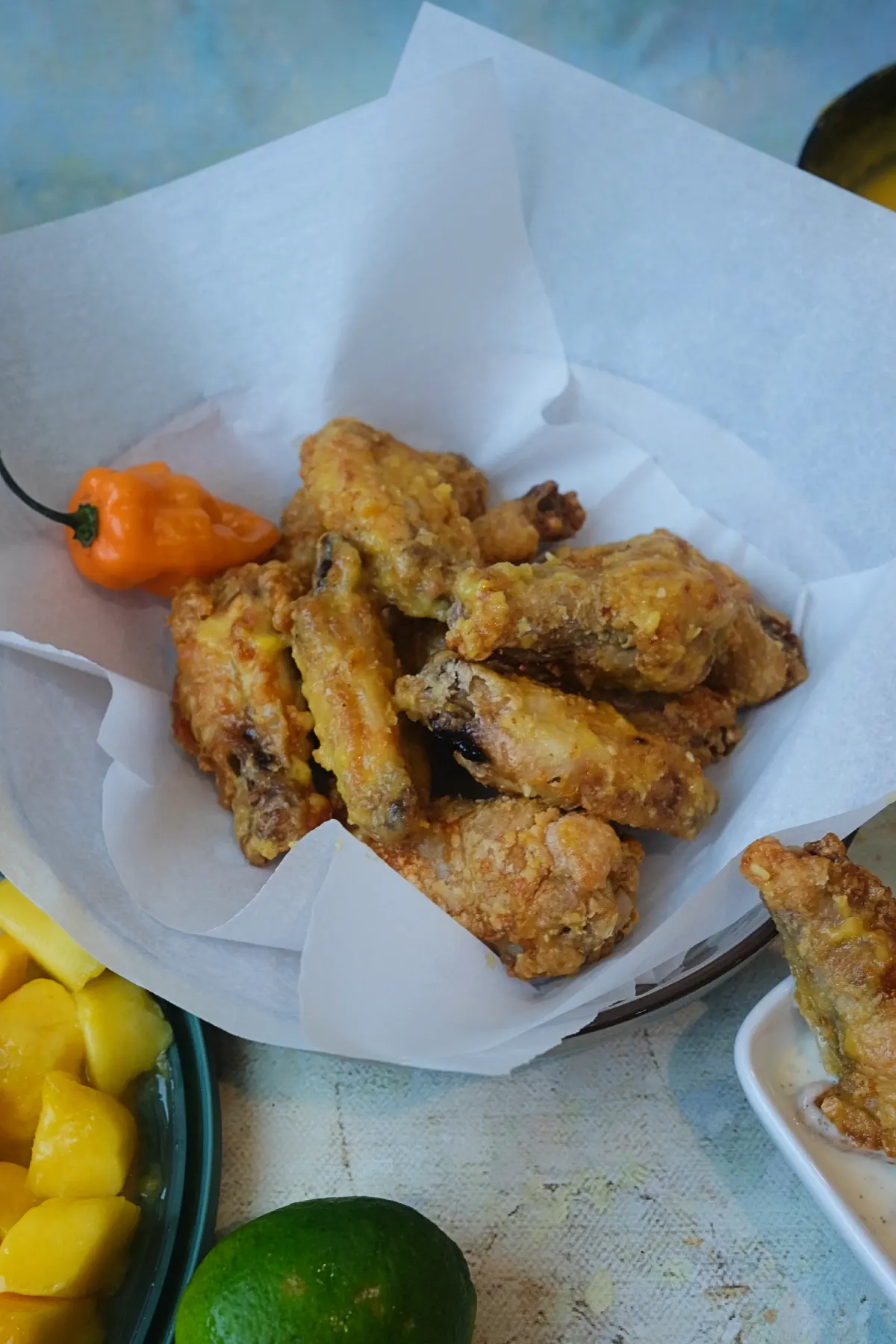 Parchment-lined bowl filled with crispy mango habanero wings beside ranch dip and fresh habanero peppers.