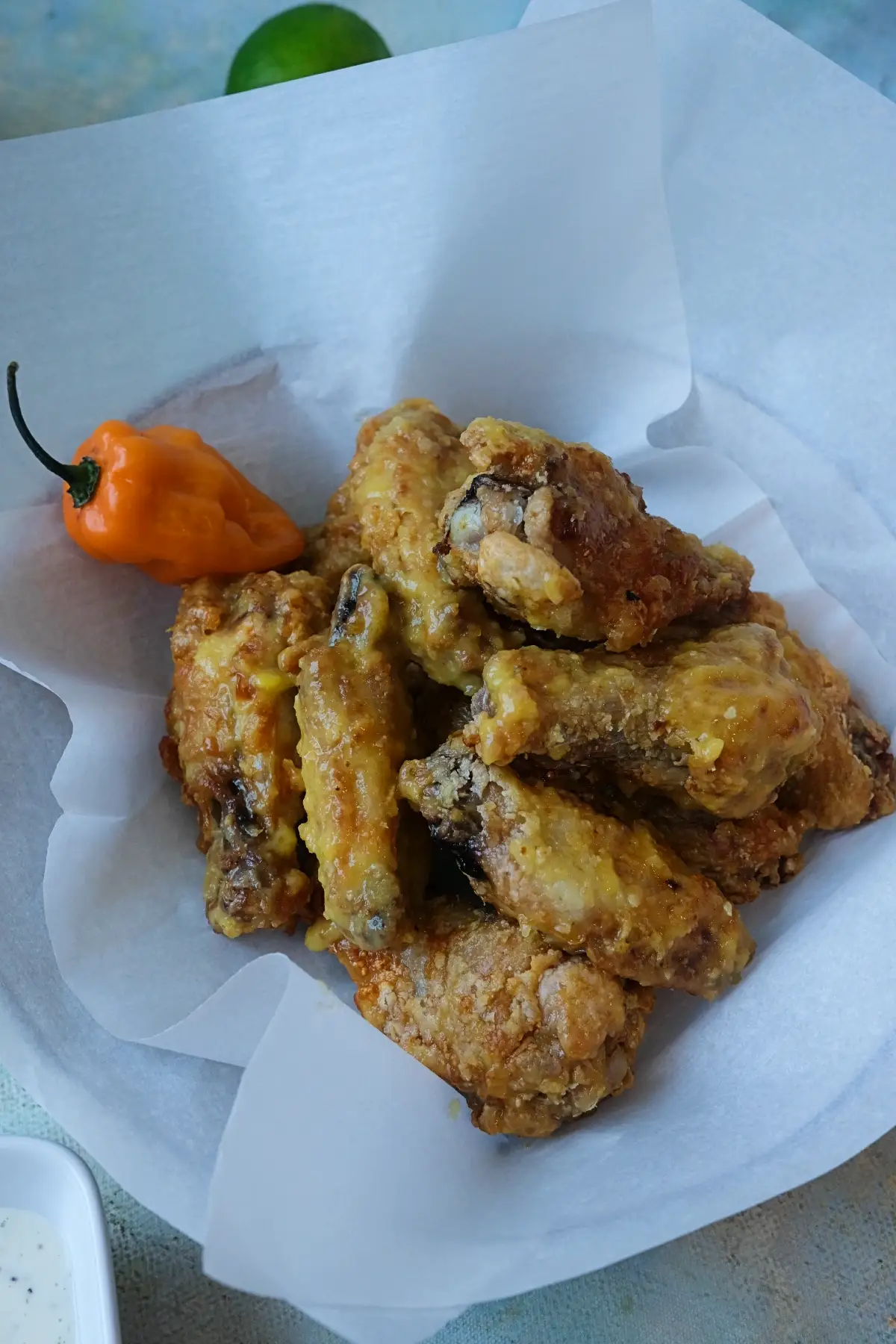 Overhead view of mango habanero wings in a bowl with lime, mango chunks, sauce, and ranch dip nearby.