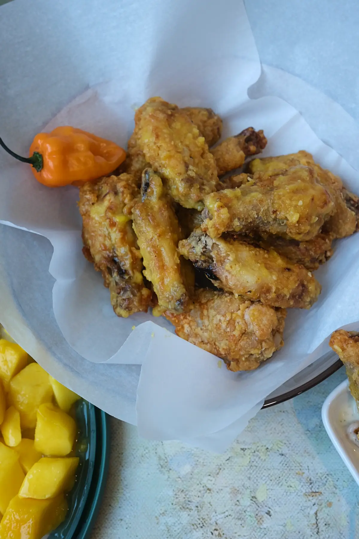 Parchment-lined bowl filled with crispy mango habanero wings beside ranch dip and fresh habanero peppers.