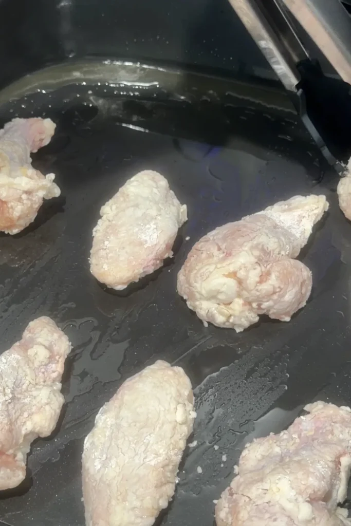 Flour-coated chicken wings placed inside an air fryer basket before cooking until crispy.