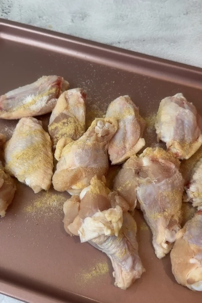 Raw chicken wings sprinkled with salt, garlic powder, and pepper.