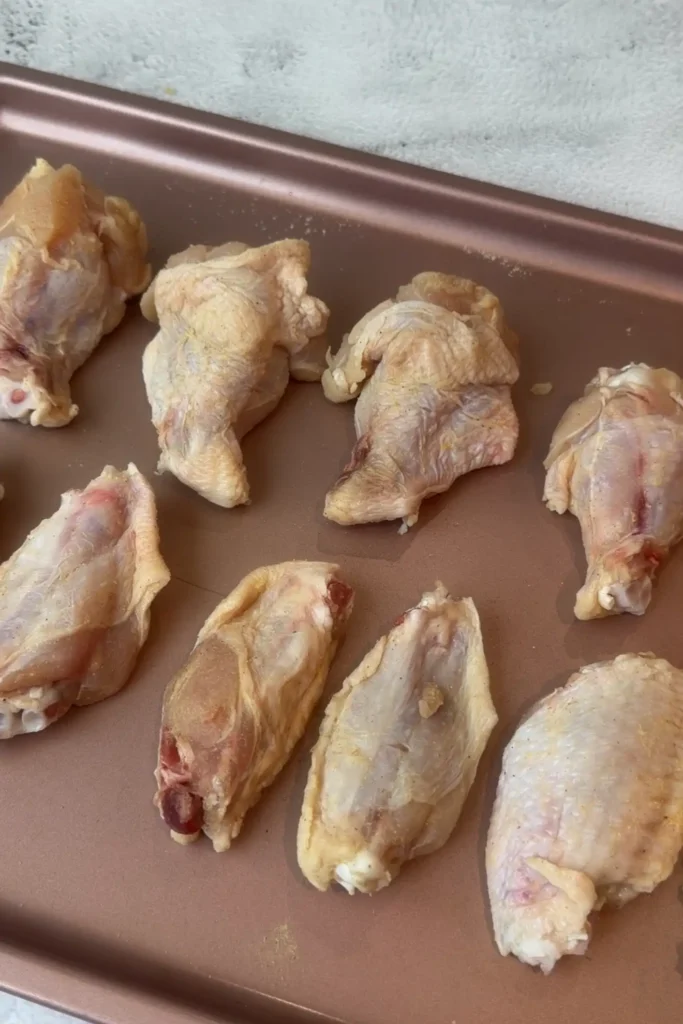 Seasoned chicken wings resting on a baking sheet before coating.