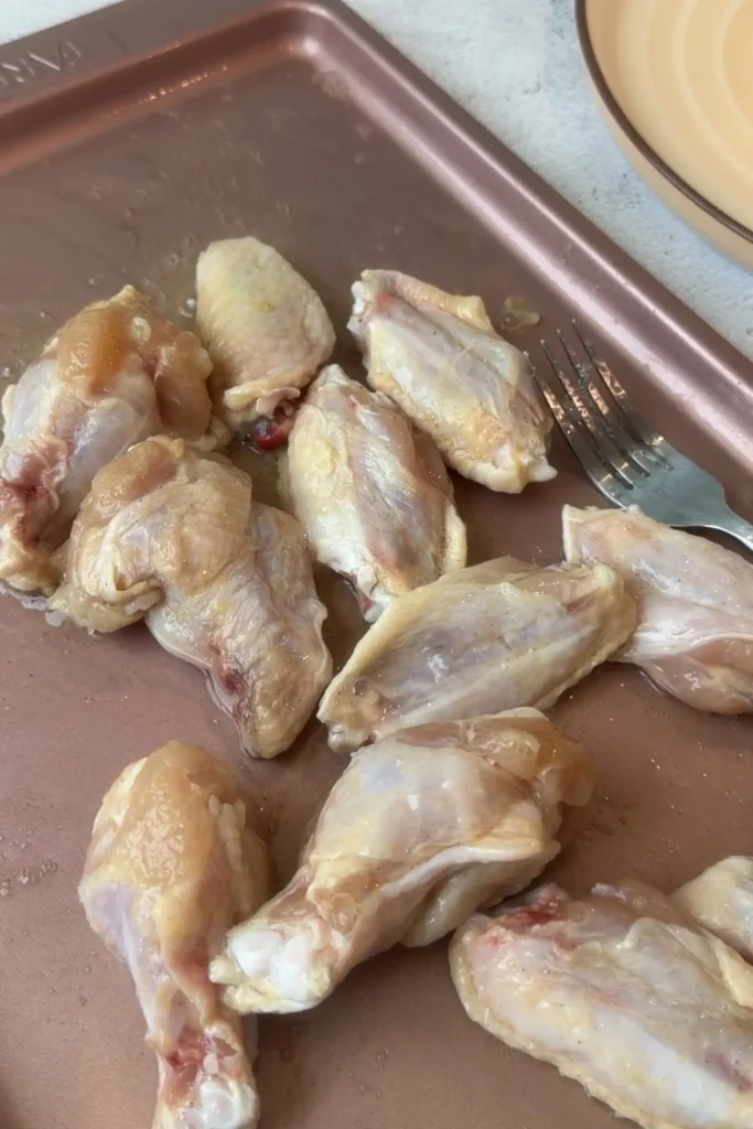 Raw chicken wings coated in egg whites and seasoning on a baking sheet.