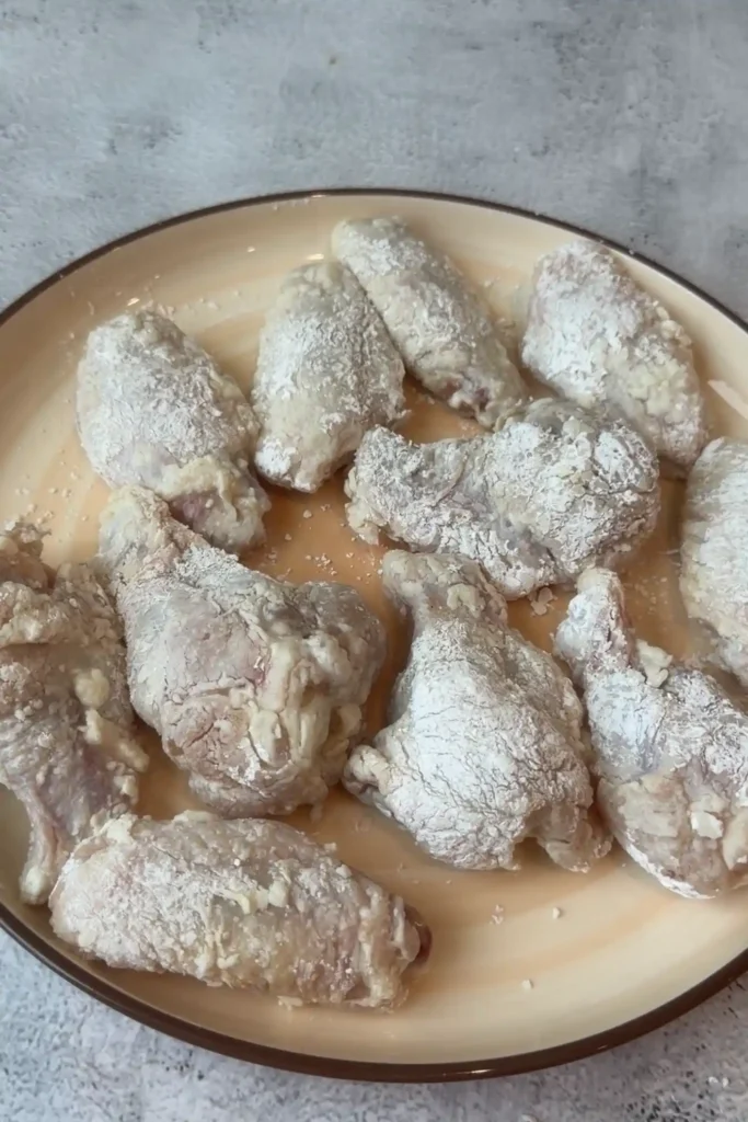 Cornstarch-coated chicken wings resting on a plate before air frying.