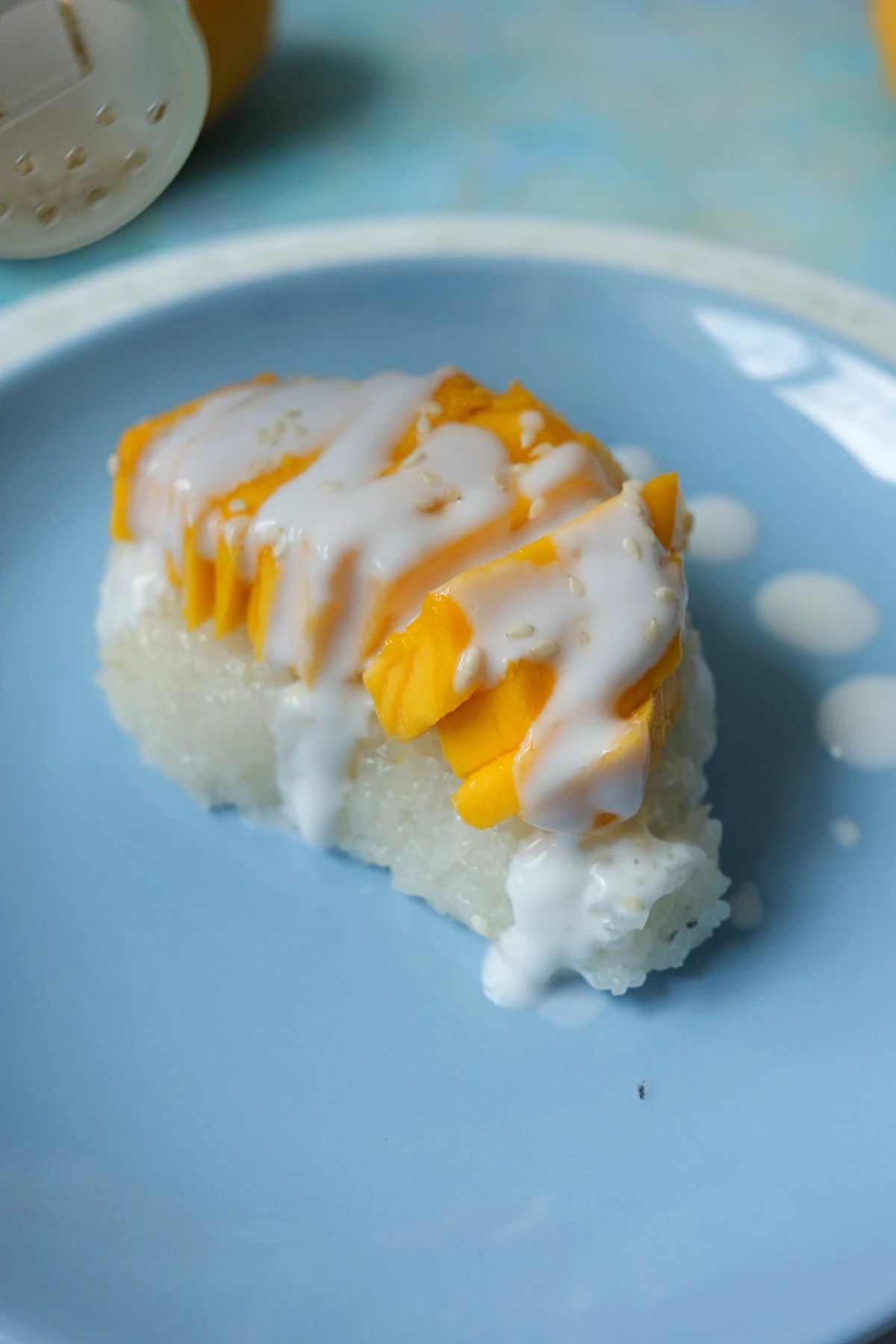 Mango sticky rice topped with sliced Manila mangoes, coconut sauce, and sesame seeds on a blue plate.