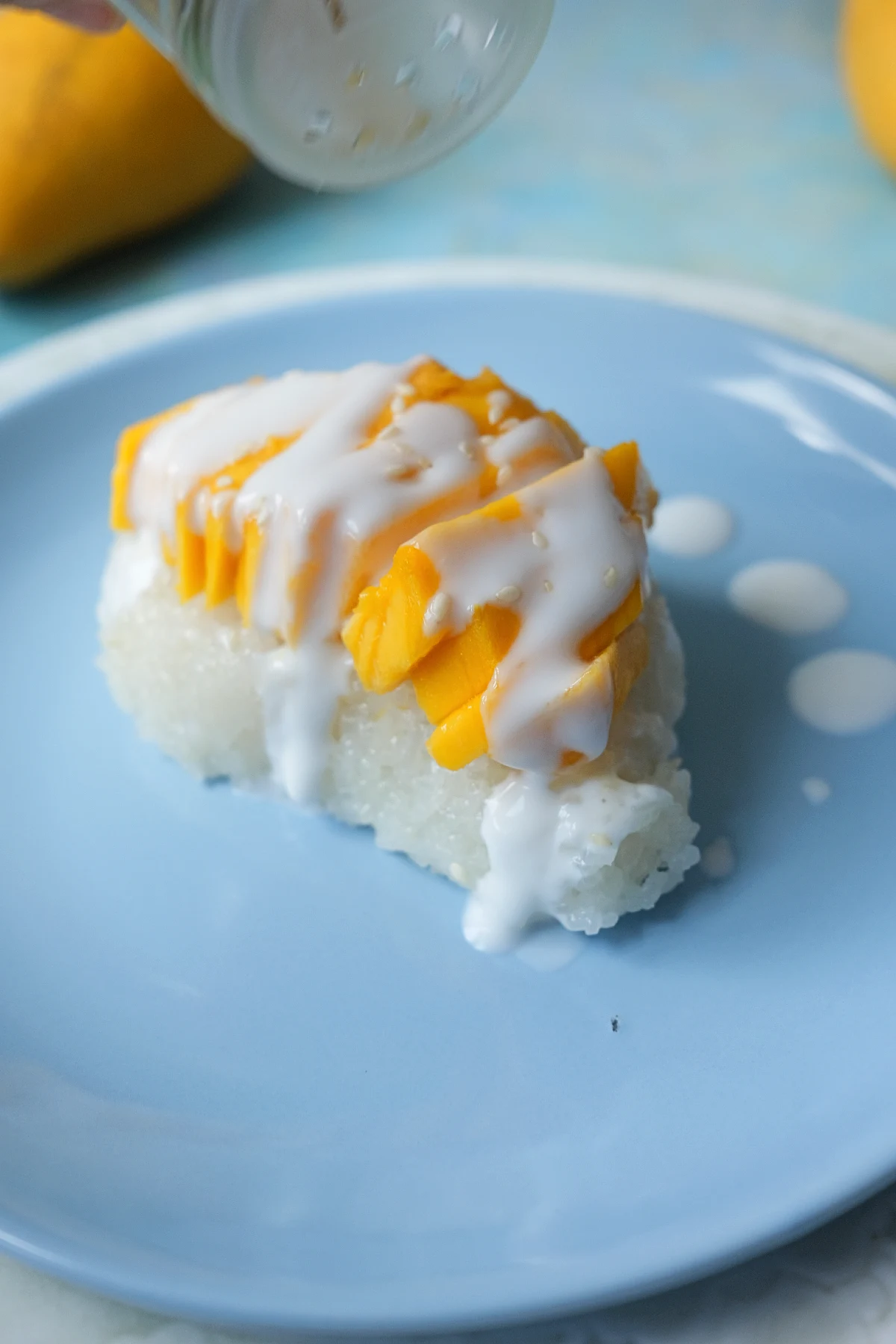 Sesame seeds being sprinkled over mango sticky rice topped with fresh sliced mangoes.