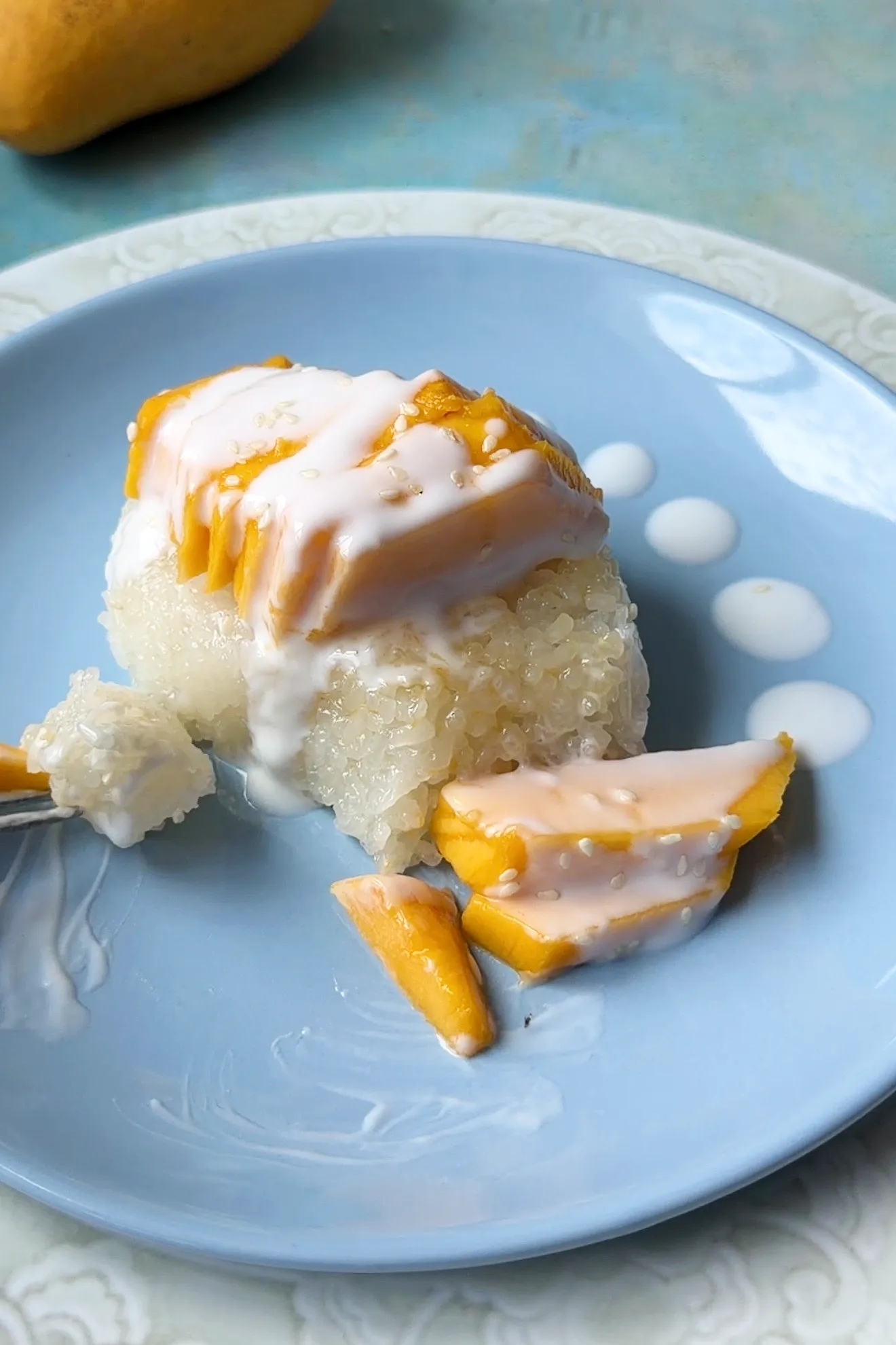 Close-up of mango sticky rice with creamy coconut sauce, sesame seeds, and sliced fresh mangoes.