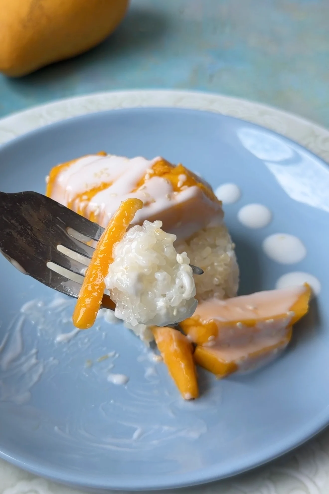 Fork lifting a bite of sticky rice and mango coated with coconut sauce and topped with sesame seeds.
