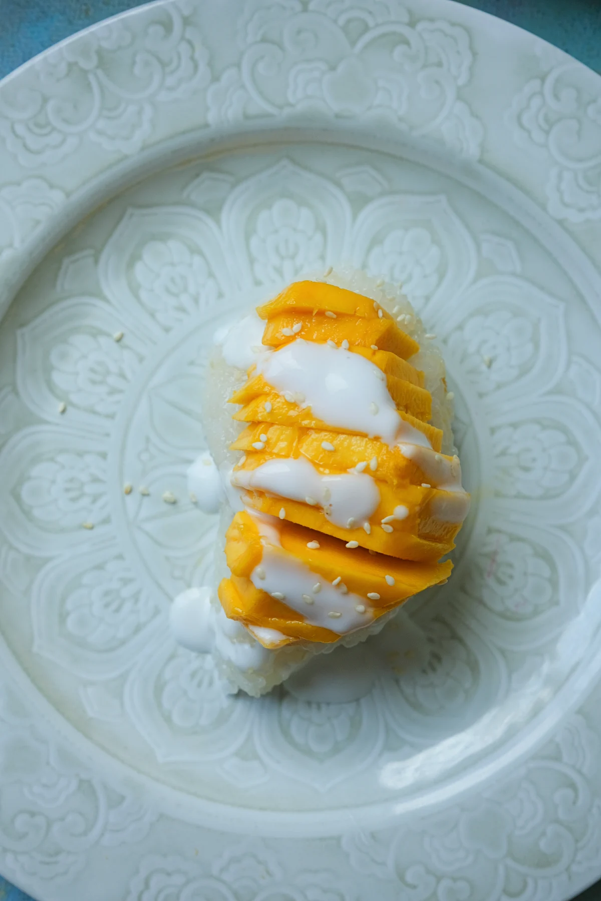 Top-down view of mango sticky rice garnished with sliced mangoes, coconut sauce, and sesame seeds.