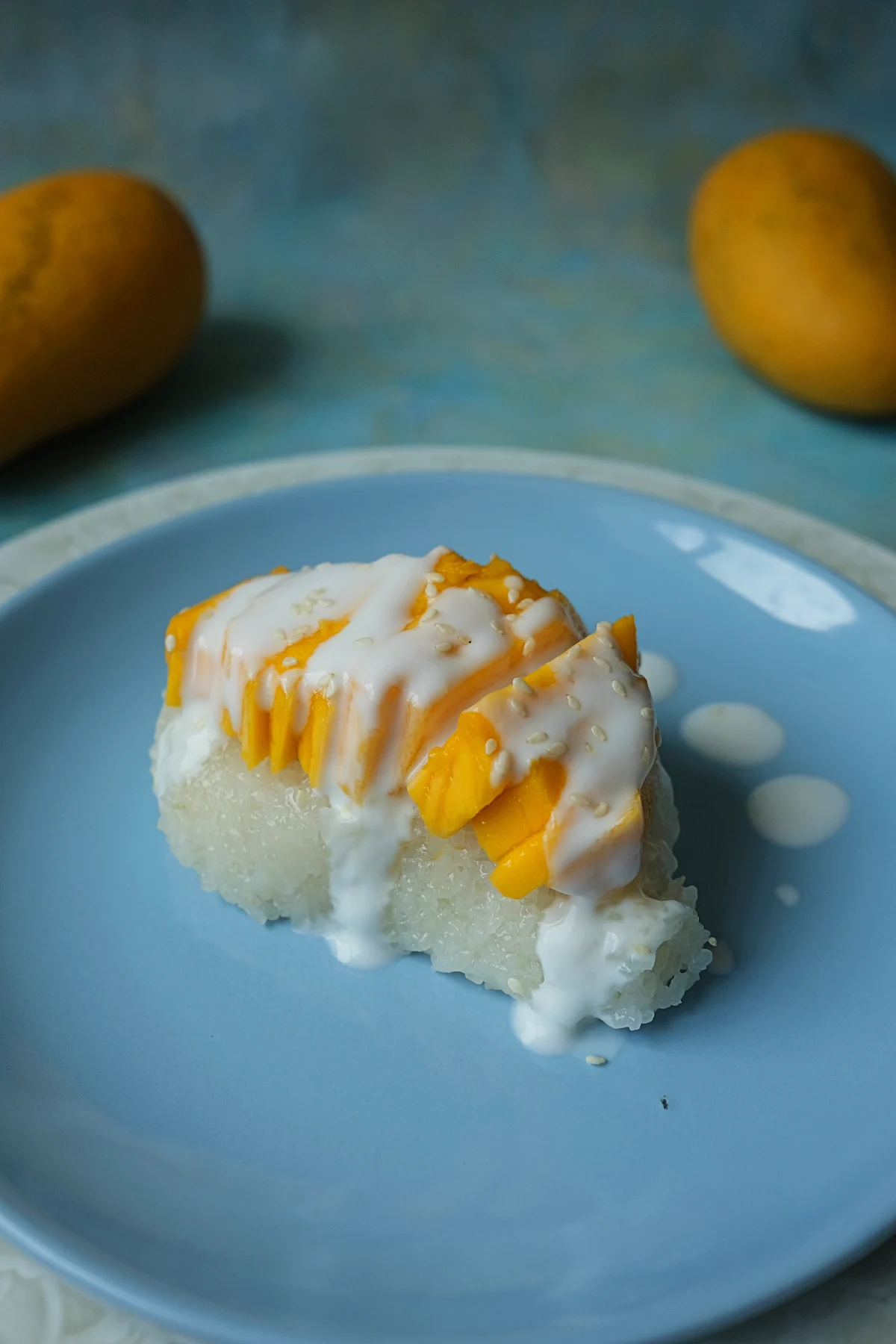 Thai mango sticky rice served with ripe Manila mangoes, coconut sauce, and sesame seeds on a blue plate.