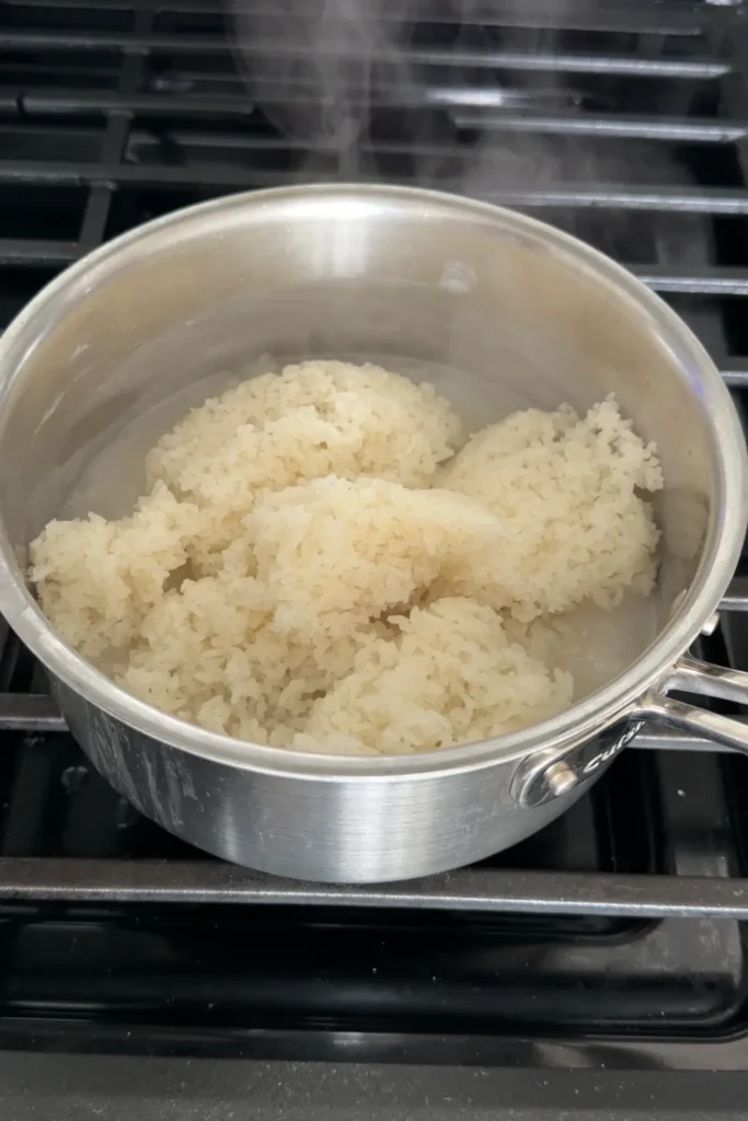 Freshly steamed glutinous rice added to the warm sweetened coconut milk mixture in a saucepan