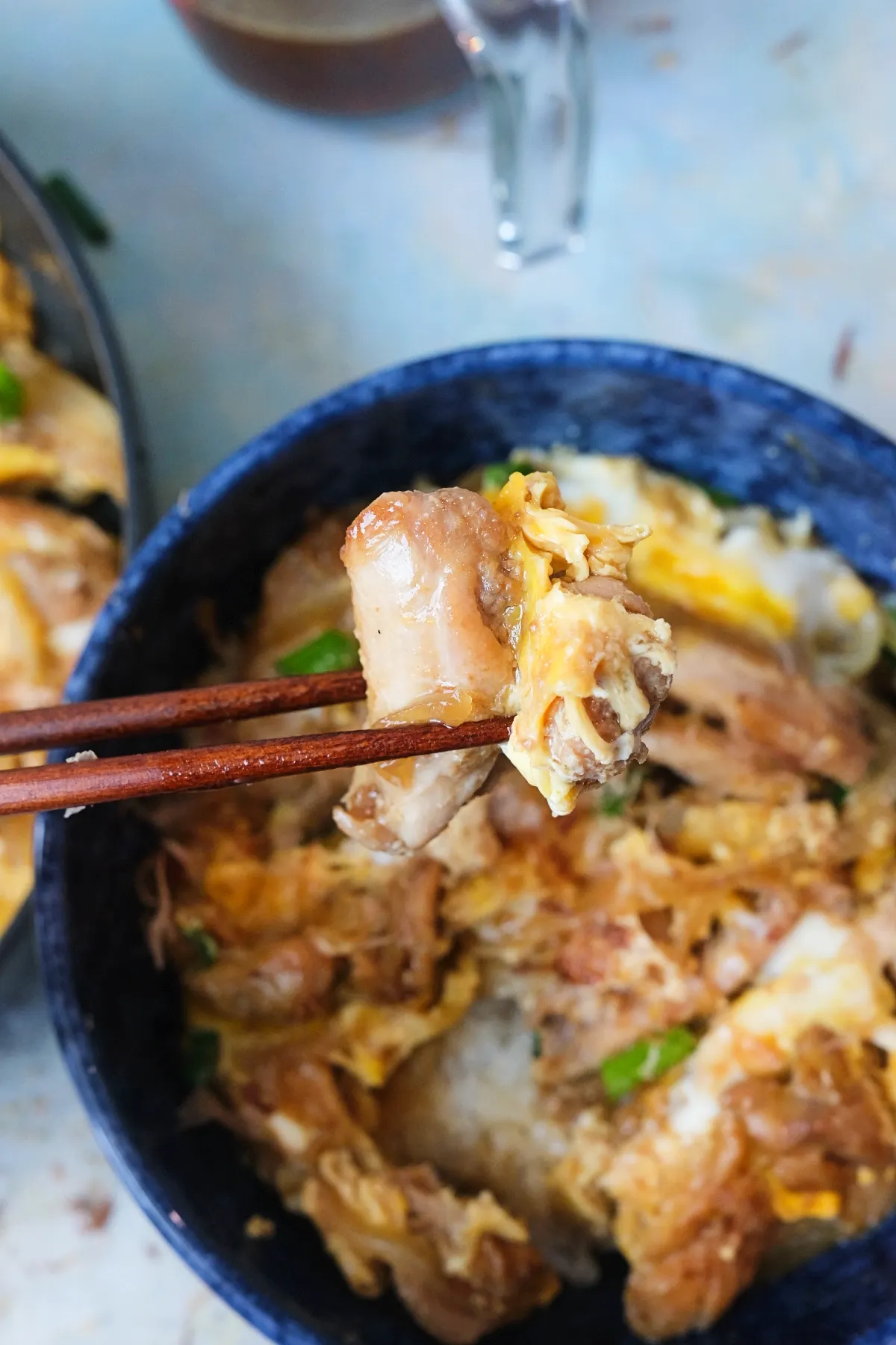 Chopsticks holding a bite of chicken and egg from a bowl of oyakodon, showing the tender texture and sauce.