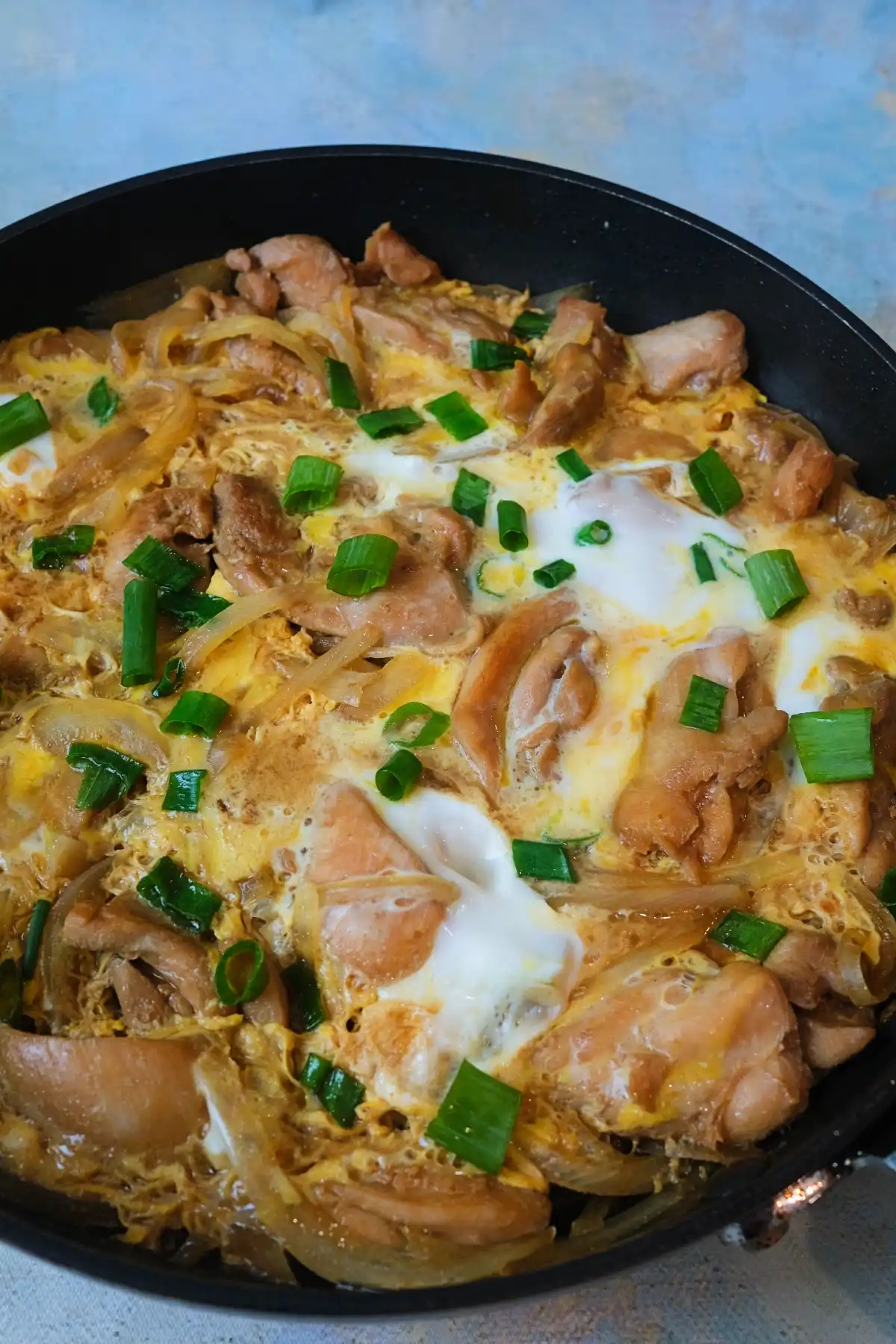 Oyakodon in a pan topped with chicken, soft eggs, green onions..