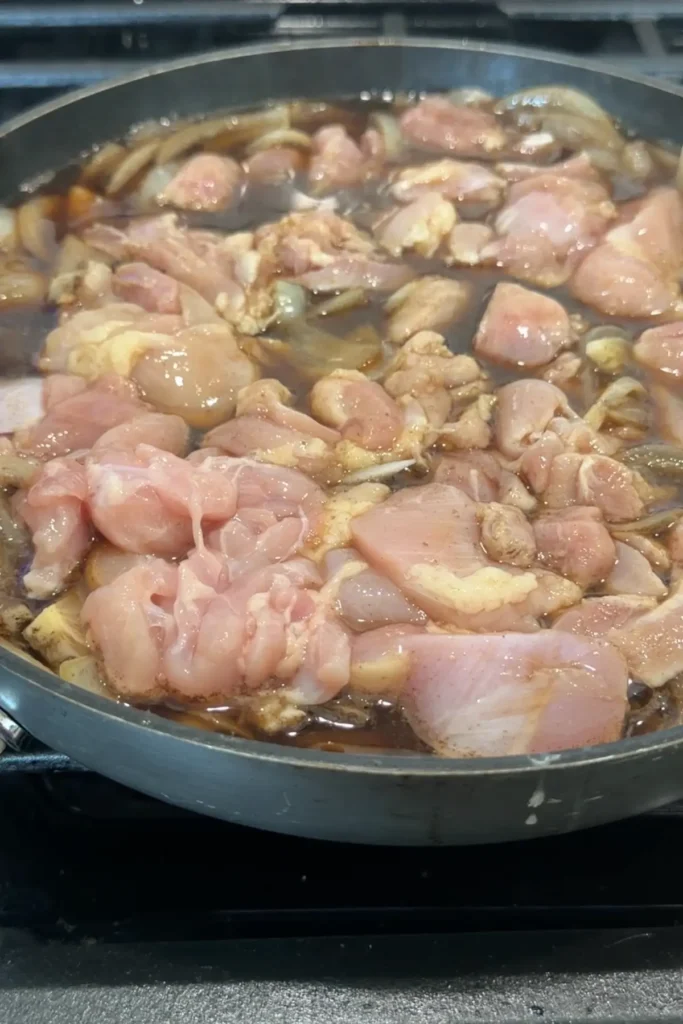 Raw chicken pieces added to the pan with simmering onions and sauce.