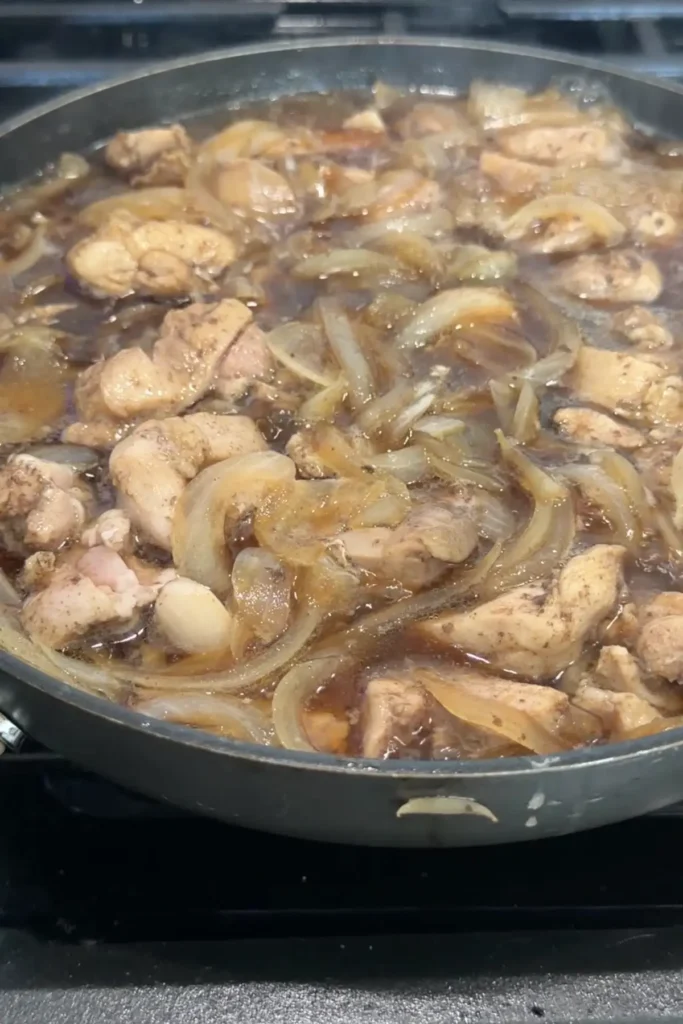 Chicken and onions cooking together in a savory soy-based sauce.