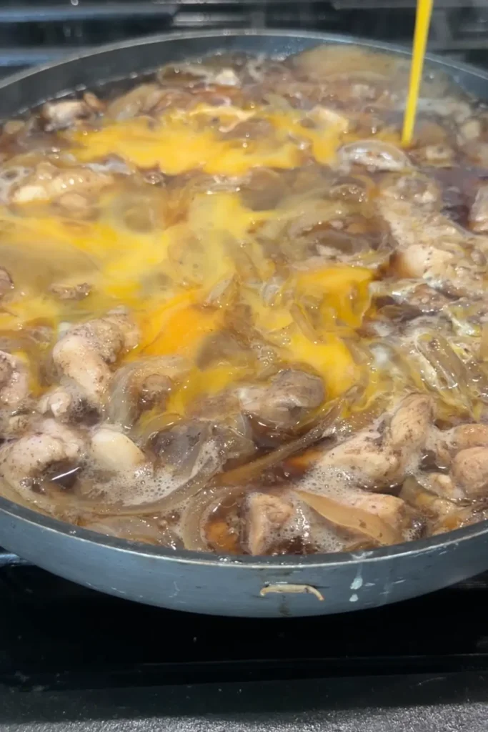 Beaten eggs being poured into the pan over simmering chicken and onions.