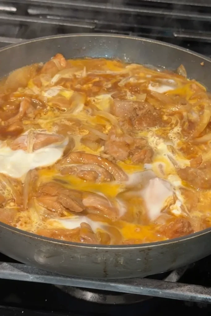 Eggs gently setting in the pan with chicken and onions in sauce.