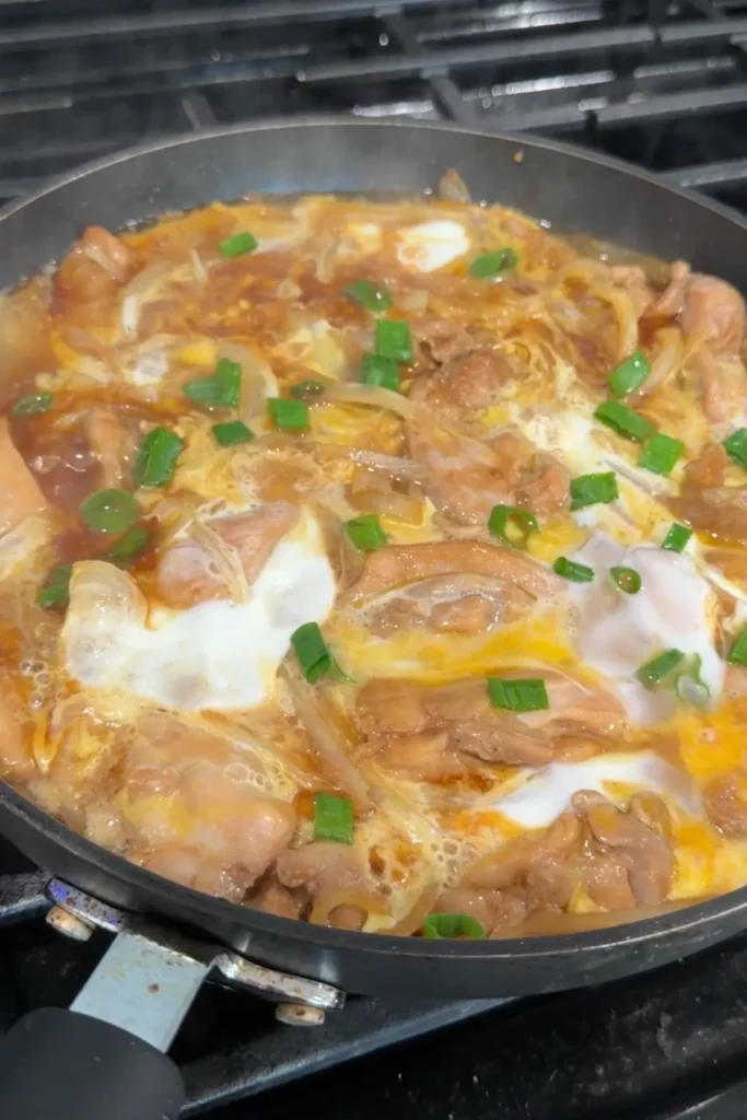 Oyakodon finishing in the pan with softly set eggs and chopped green onions on top.