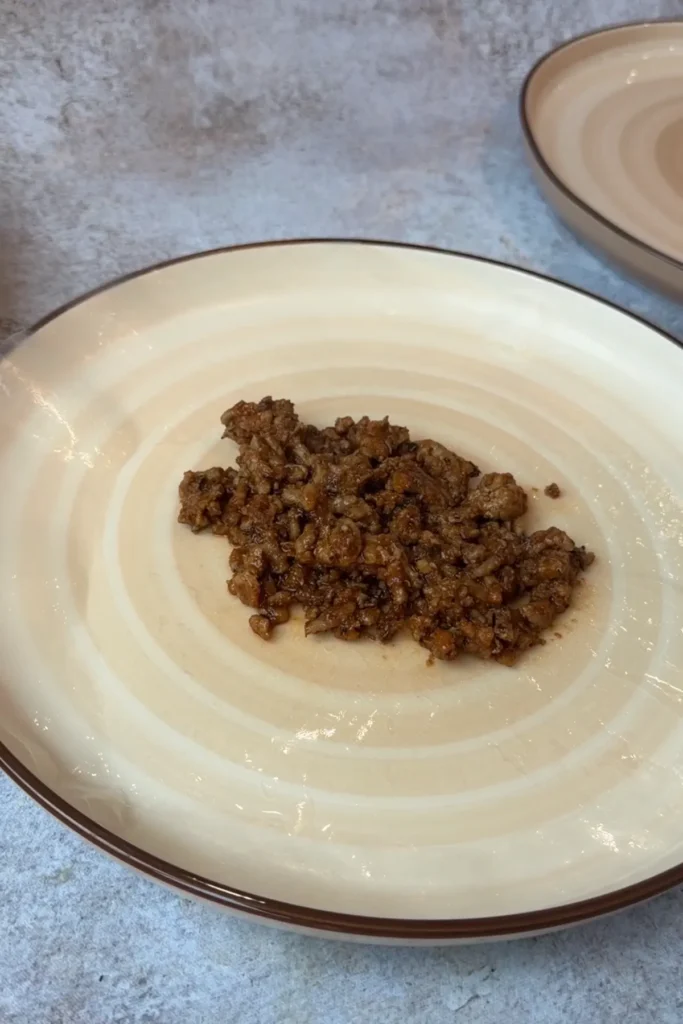 Savory pork filling placed onto softened rice paper wrapper before adding cheese.