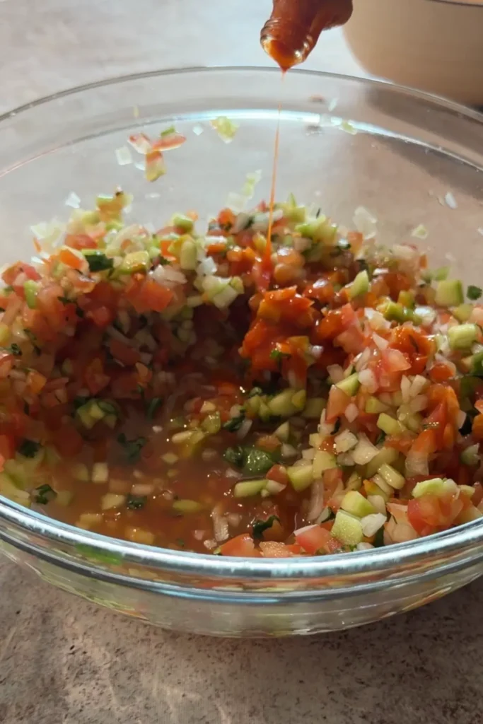Hot sauce being poured into homemade chunky salsa for extra spice.