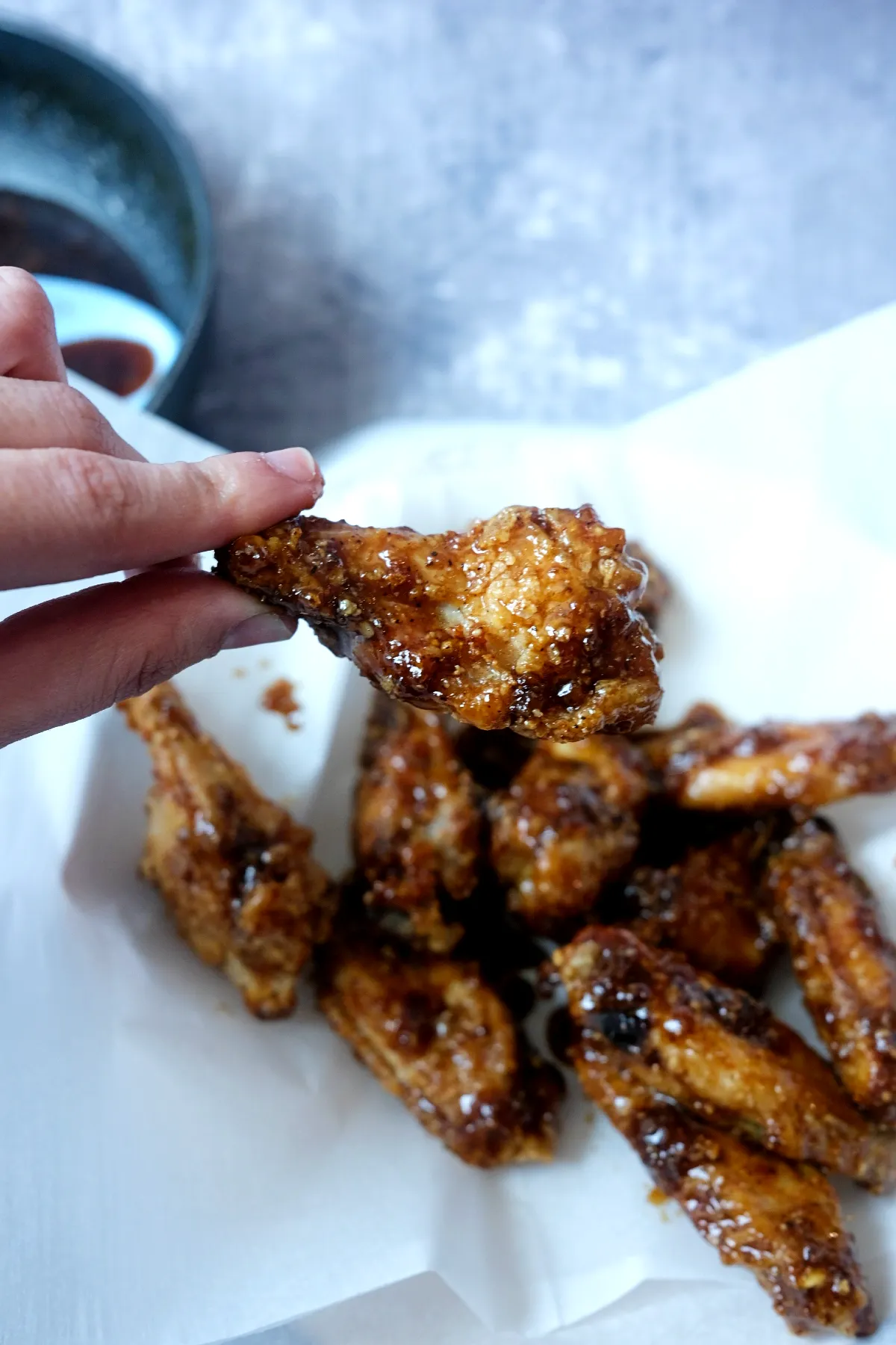 Hand holding a crispy soy garlic chicken wing coated in shiny Korean-style sauce.