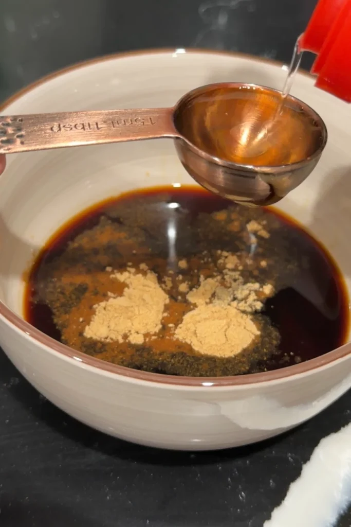 Rice vinegar pouring into a bowl of soy garlic wing sauce ingredients.
