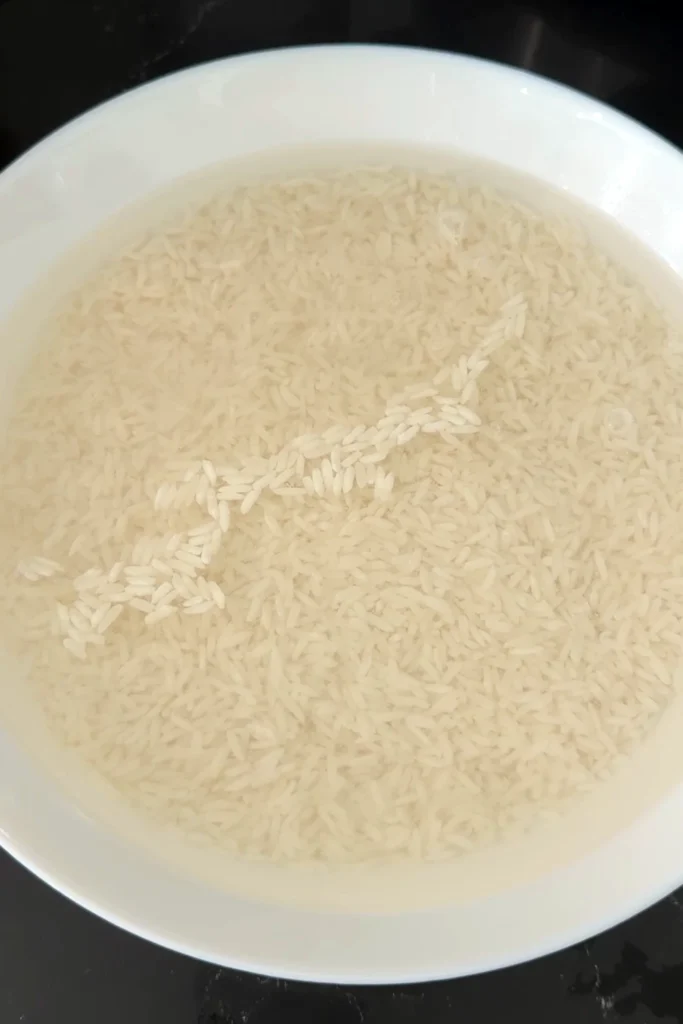 Raw glutinous rice submerged in water during the soaking process.