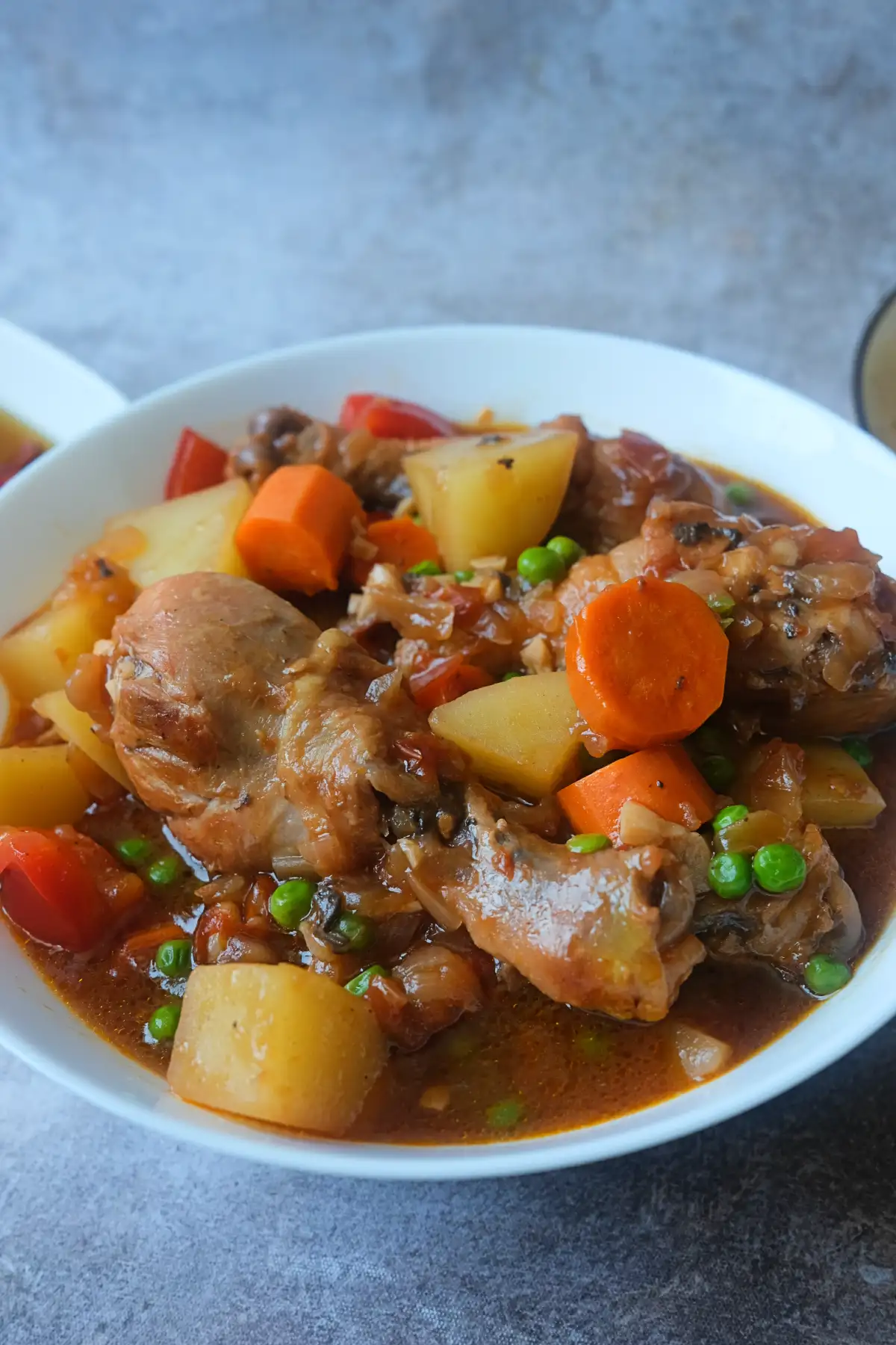 Close-up of homemade Filipino Chicken Afritada with juicy chicken drumsticks and vegetables in savory tomato sauce