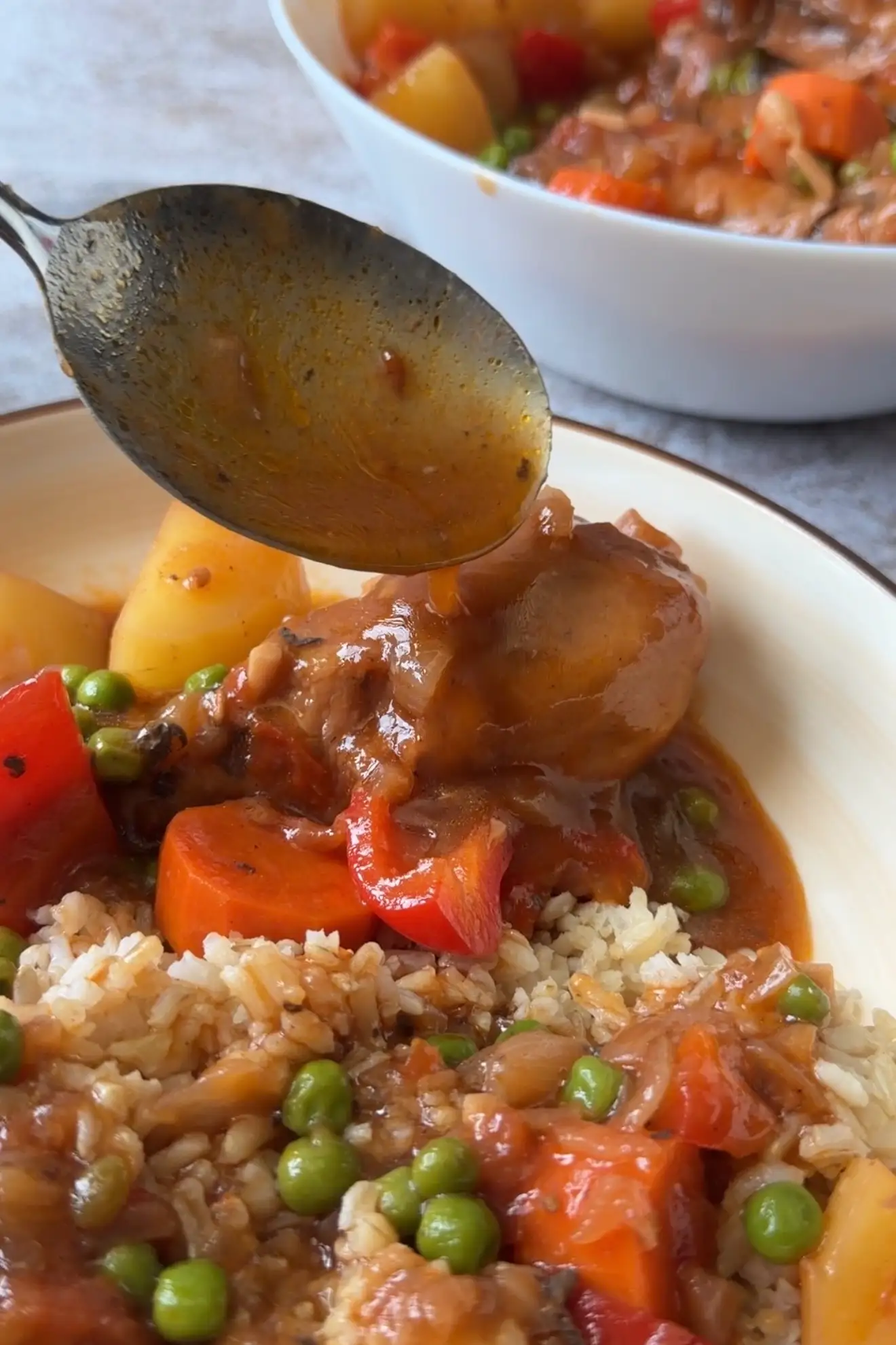 Spooning rich tomato sauce over Chicken Afritada and brown rice for a classic Filipino meal